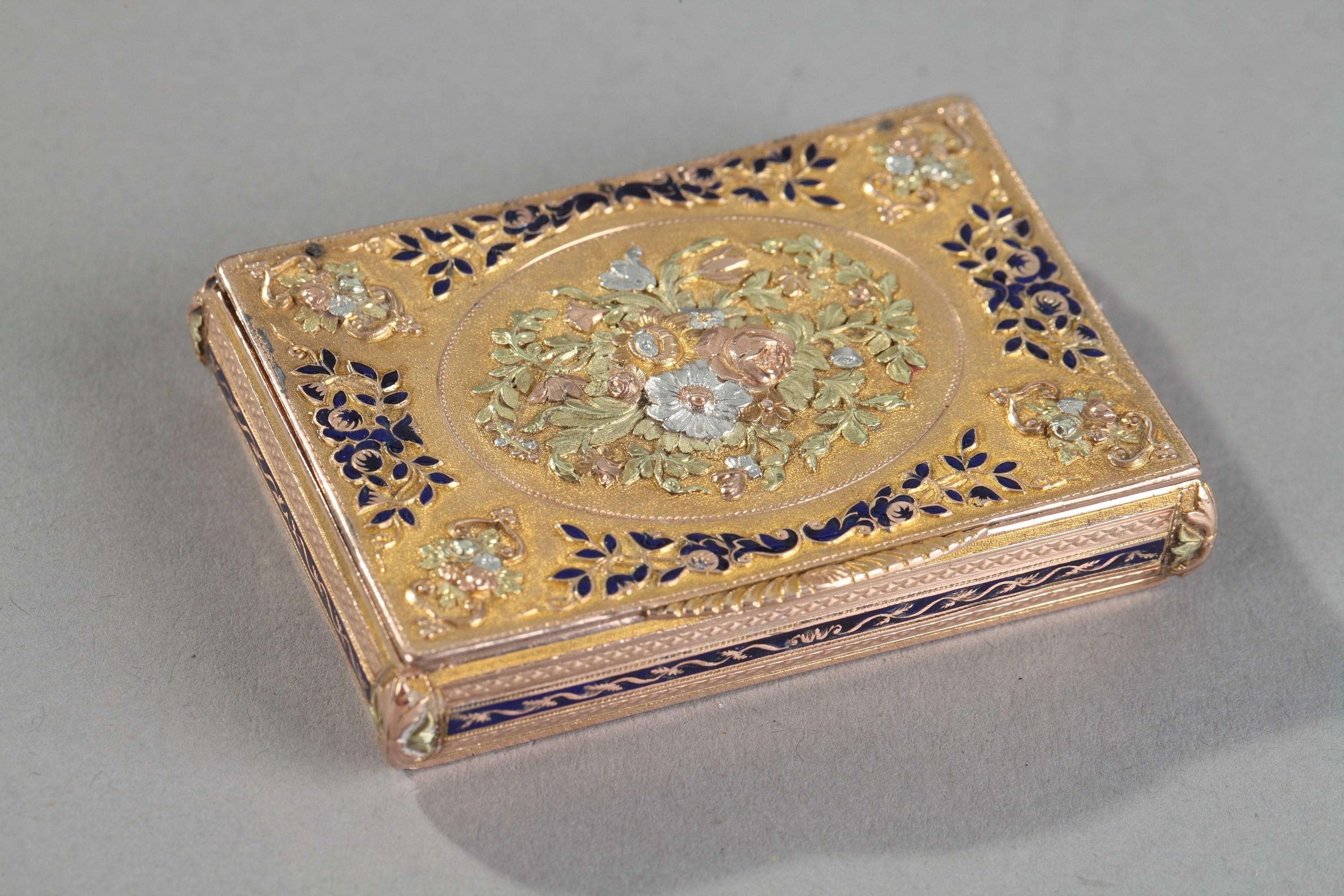 Rectangular box with three tones of gold and royal blue enamel. The hinged lid is embellished with a multicolored gold medallion in relief featuring a bouquet of roses and tulips, set on a matte gold background. Delicate foliage accented with royal