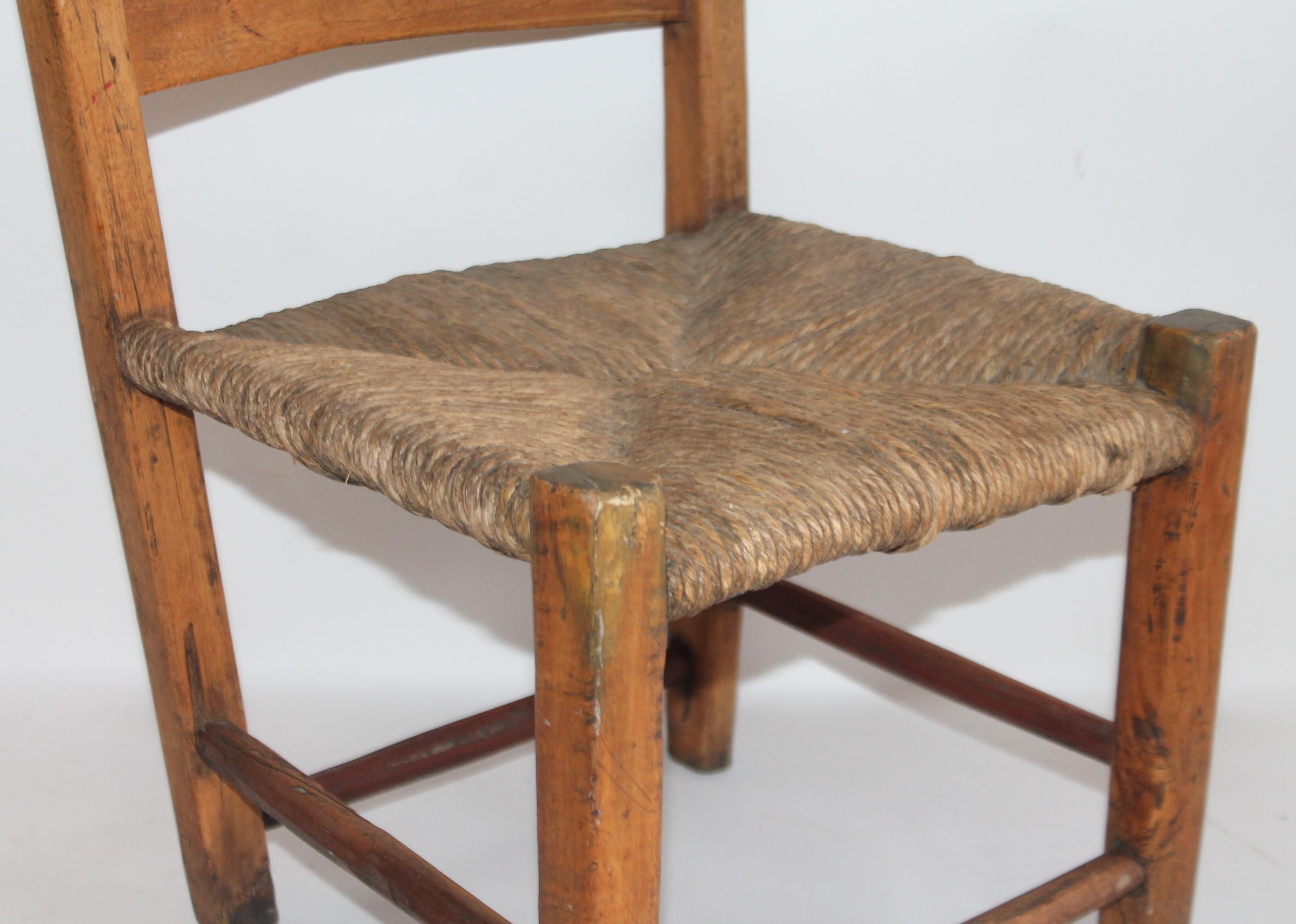 This early form strong and very sturdy child's ladder back chair from New England is in fine and worn condition. The rush seat is very strong and sturdy with a fantastic patina.