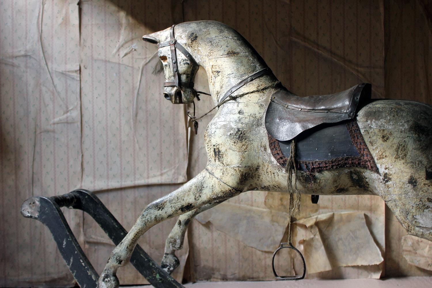 The large and early 19th century dappled grey rocking horse on bow rocker, at almost seven feet wide, the well carved painted and gessoed horse having pricked ears, flared nostrils and open mouth, the eye sockets vacant, the body with a leather and