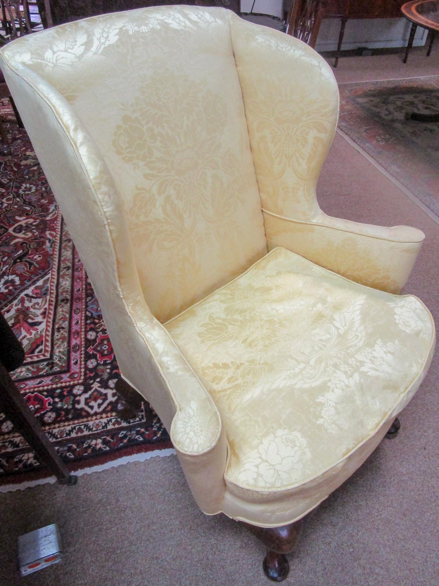 This graceful English Queen Anne wingback chair features gorgeous pale lemon damask upholstery with a loose, down cushion stuffing. It is unique to find a Queen Anne walnut cabriole leg ending in pad feet in both the front and in the back of the