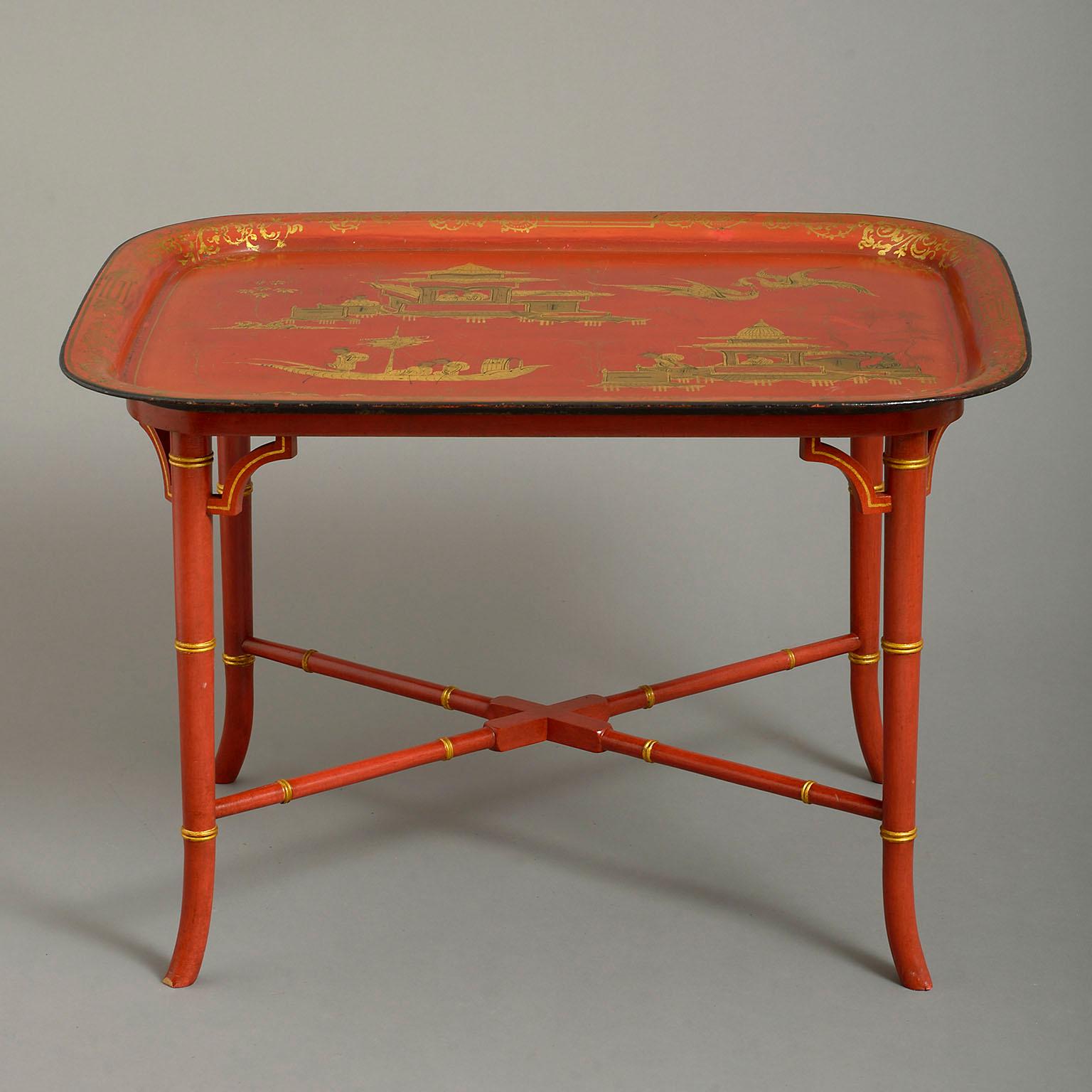 An early 19th century Regency japanned tole tray forming a coffee table, decorated with chinoiserie scenes on a sealing-wax red ground and with later conforming vogue Regency stand.