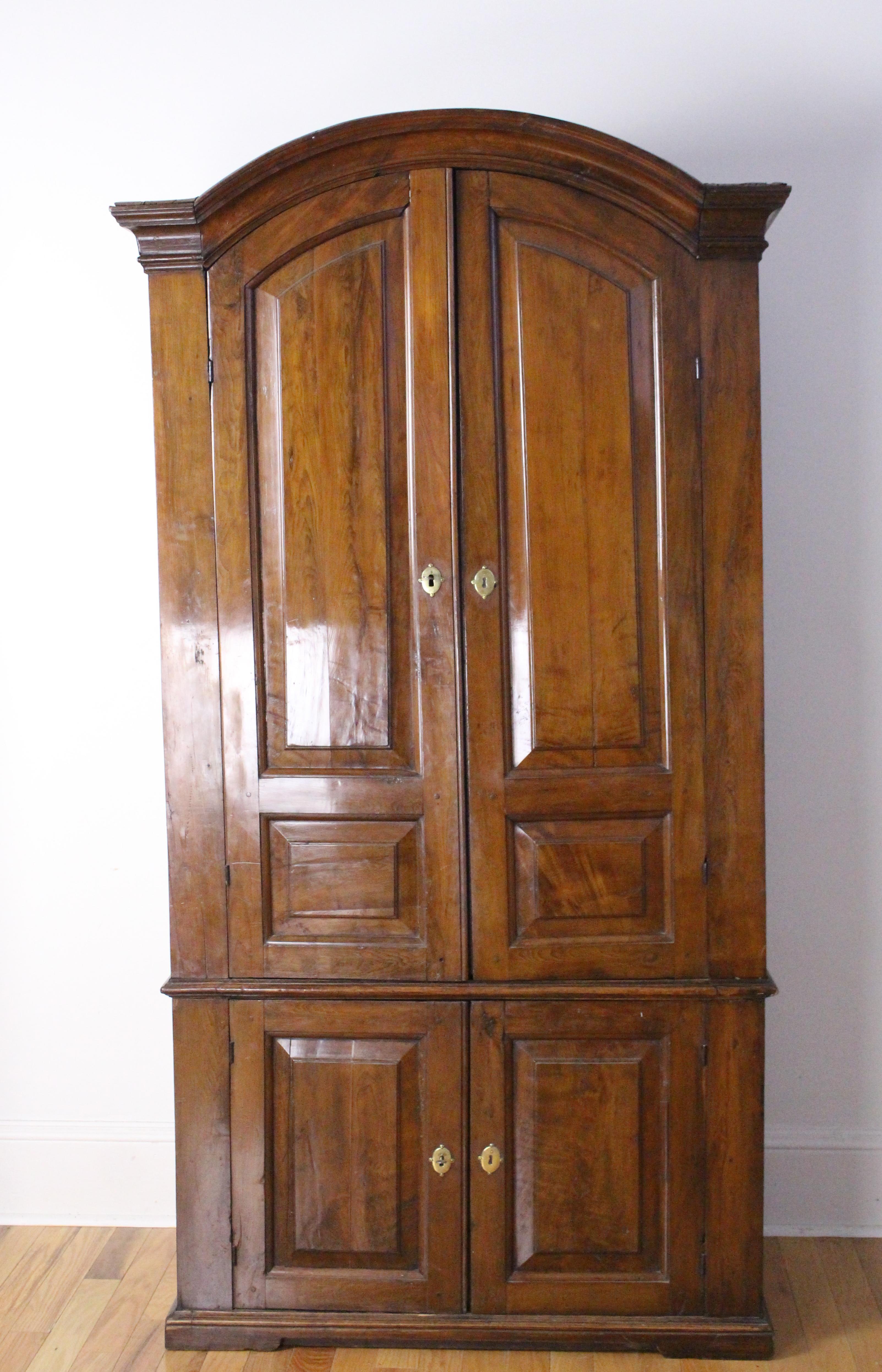 A large and imposing yew cupboard with graceful lines, wonderful rich color and very good patina. Good roomy storage piece with keys for both upper and lower cabinets. The piece has two issues. Though we have tried, we cannot quite correct the