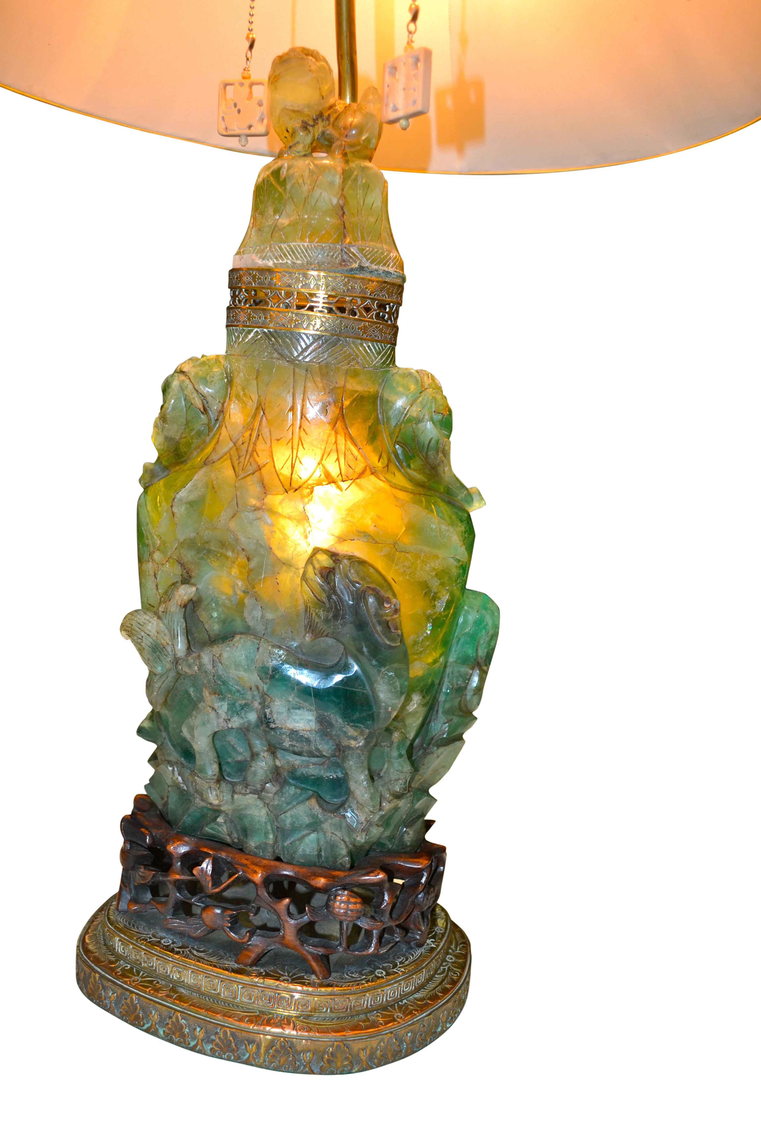 Une lampe chinoise relativement grande en pierre sculptée montée sur une base en laiton étagé et en bois de rose sculpté. La pierre sculptée est souvent appelée jadéite ou quartz, mais elle appartient en fait à la famille des fluorites. Sa base de