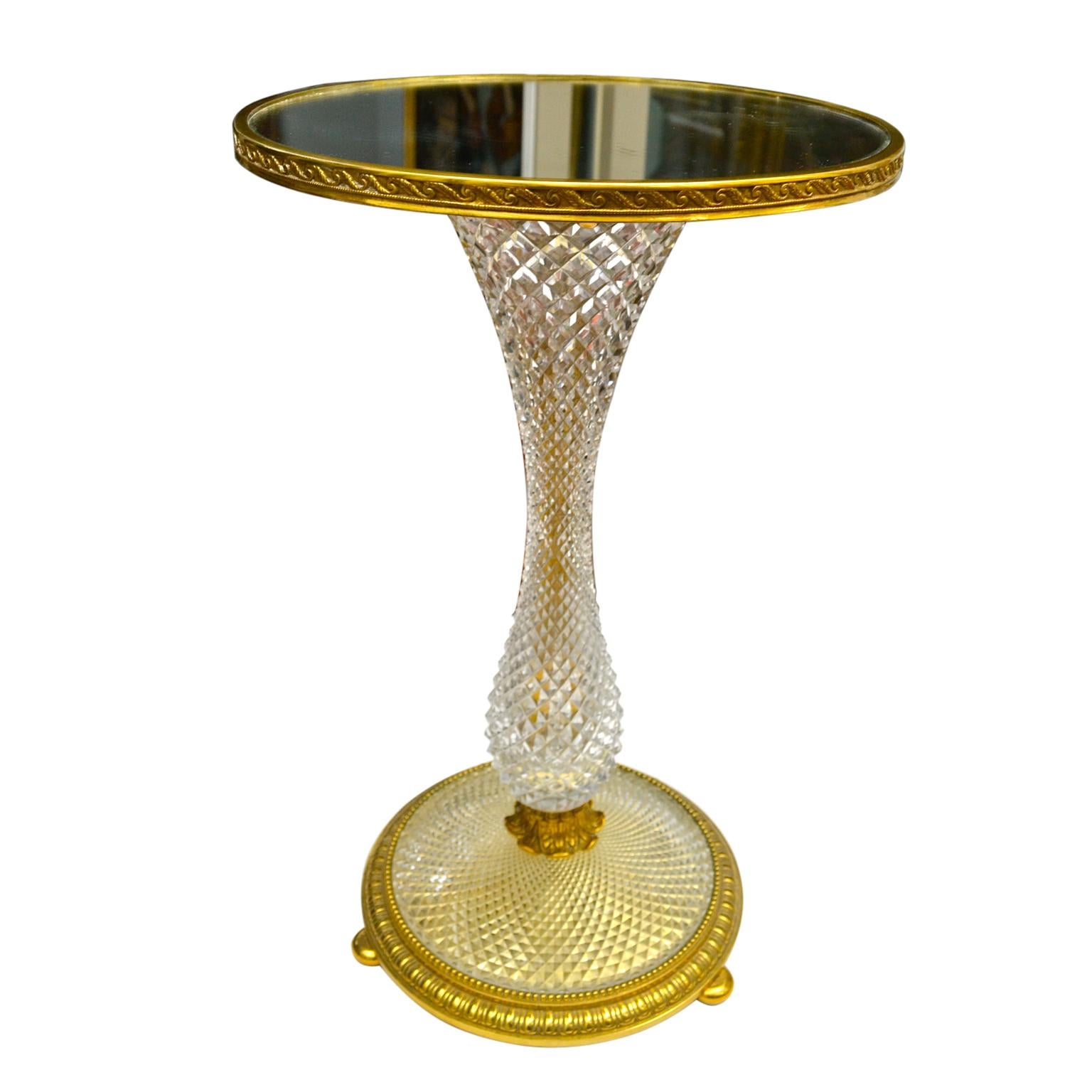 A round occasional table most likely made by the French company Baccarat in Paris at the turn of the 20th century. The mirrored top with gilt decorative banding sits on a shaped and faceted crystal 'stem' joining to a lower circular cut crystal