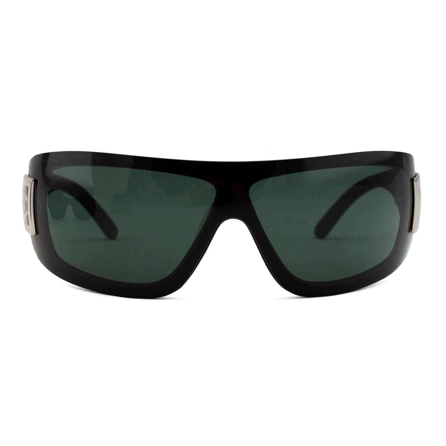 Chanel sunglasses from the early 2000's. Black resin wrap around style with contrasting silver CC logo in a silver square. Black/green lenses. Nose piece for comfort. Made in Italy. Sold without case. Style has been popularized by Sarah Jessica