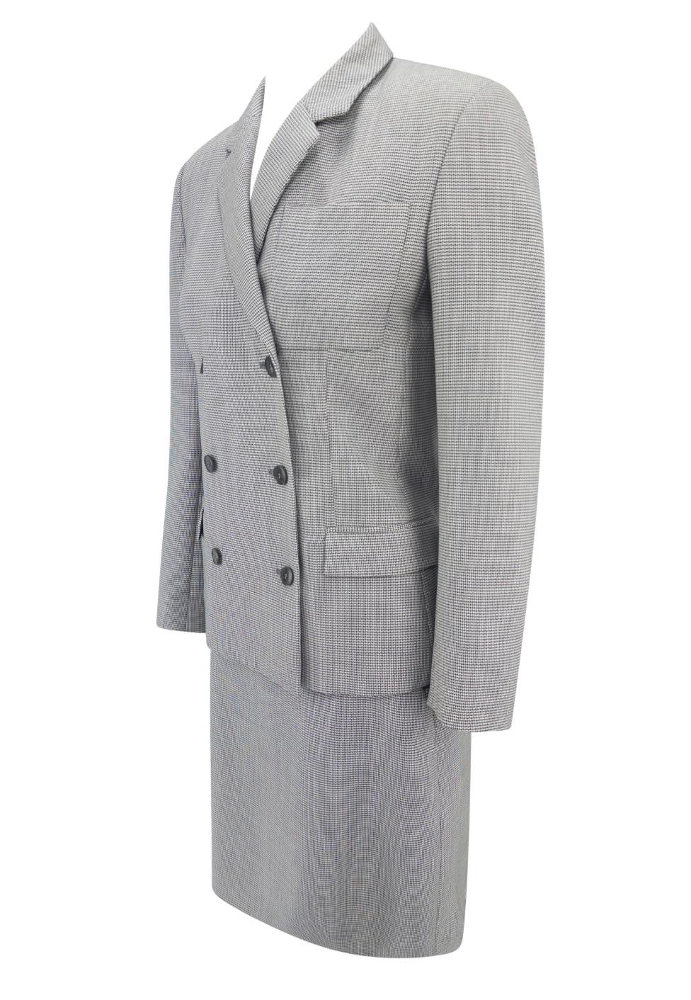 Este traje de falda Calvin Klein gris de lana y mohair de principios de la década de 2000 está confeccionado con un sutil estampado de cuadros. La chaqueta de doble botonadura tiene solapa de muesca, hombros estructurados y cintura definida, y se