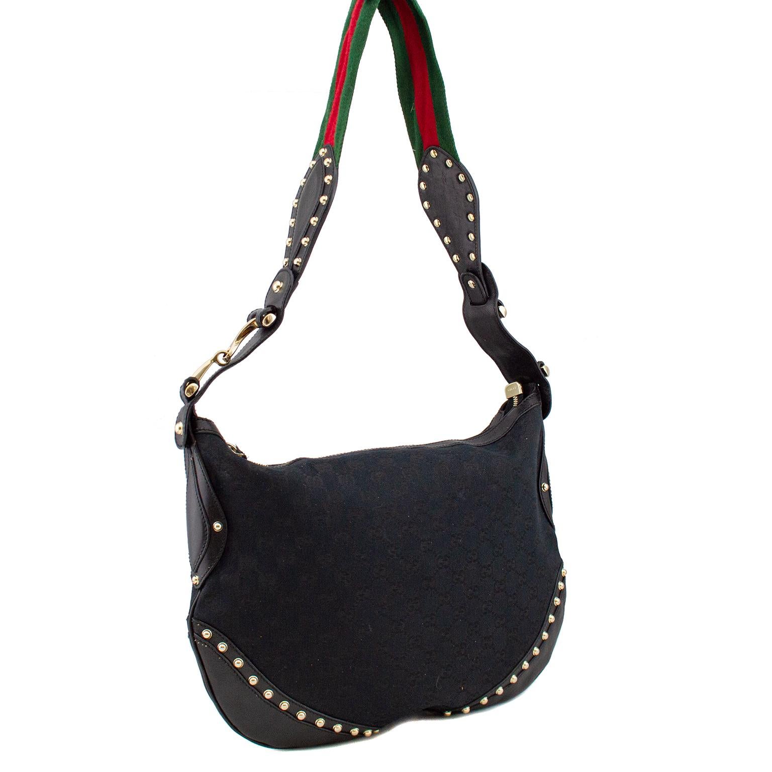 Early 2000's  Gucci black GG canvas messenger bag with gold tone metal hardware and studs, flat red and green canvas web shoulder strap, black leather trim. An updated version of the iconic Gucci horse bit on either side of strap. Black woven