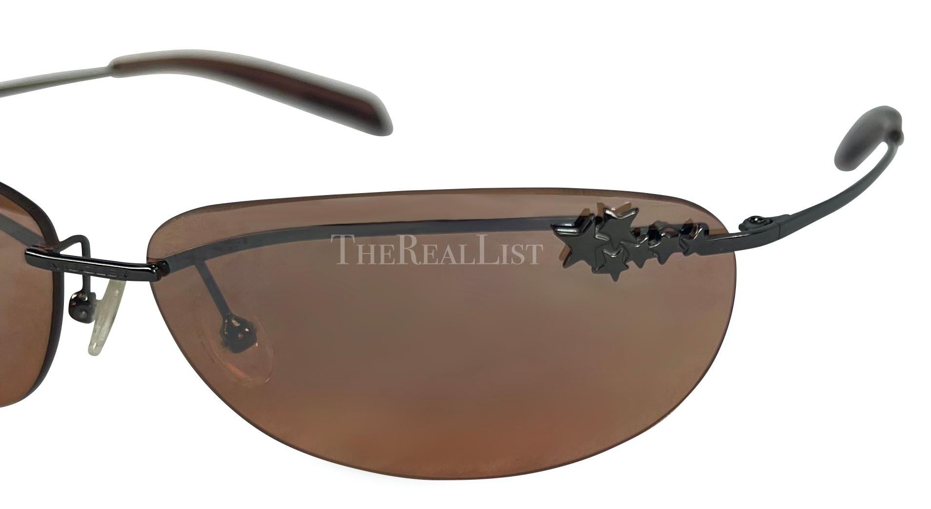 These brown Thierry Mugler sunglasses were designed by Manfred Mugler in the early 2000s. They have rimless brown-tinted lenses and thin metal arms, giving them a sleek, minimalist look. The design is distinguished by Mugler's signature star accents