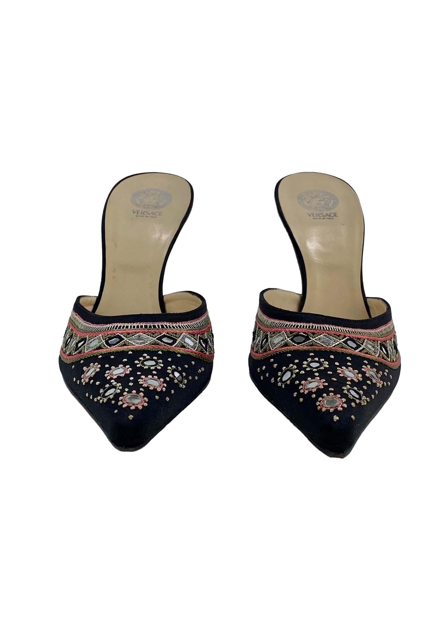 Presenting a pair of bohemian-inspired pointed Versace slide heels designed by Donatella Versace. This pair of heels is constructed of a black cloth exterior and leather interior and is embellished with small reflective mirrors and sewn embroidery.