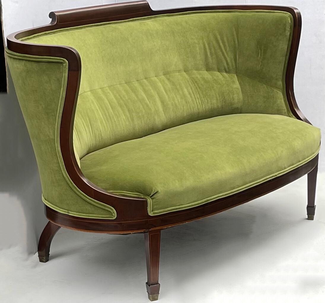 This is a beautiful classic piece. It is an early twentieth century inlaid mahogany barrelback settee upholstered in a vintage green velvet. The velvet is in very good condition.