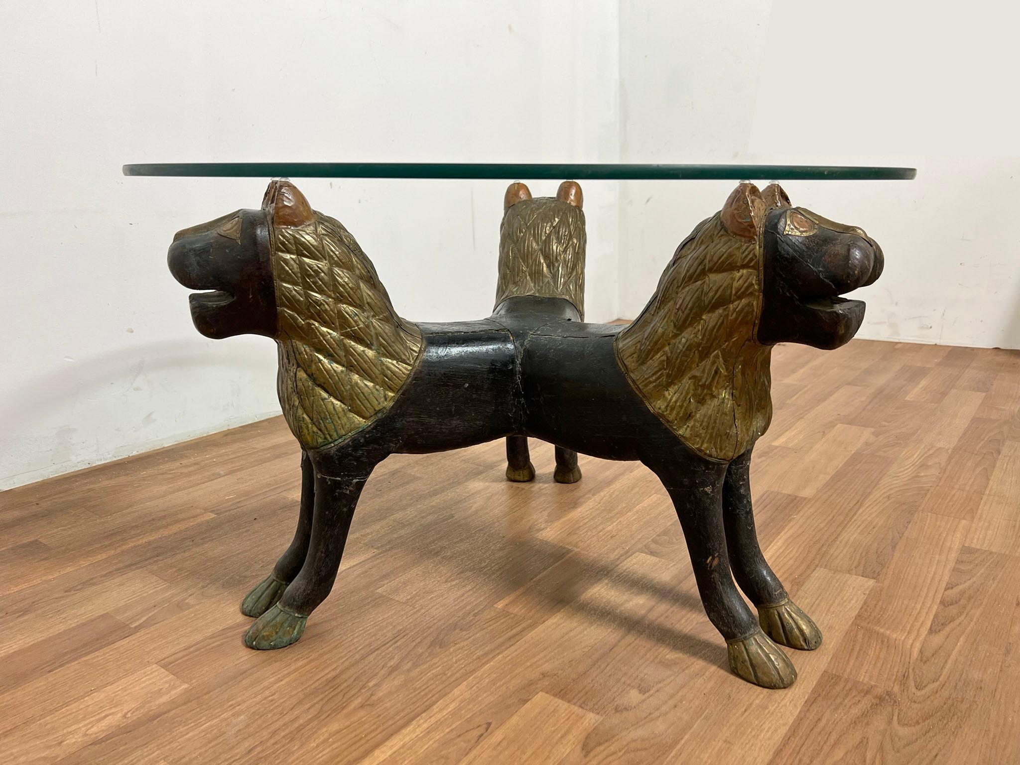 An early 20th century Anglo-Indian cocktail table of three conjoined lions in carved wood with manes and accents of sheet brass and copper in repoussé.