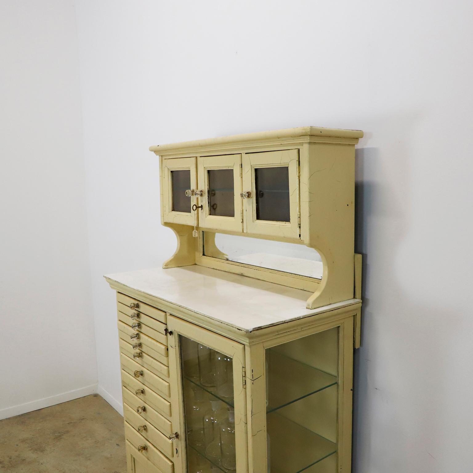 Nous vous proposons ce magnifique meuble conçu pour le secteur médical, et plus particulièrement pour les dentistes. 11 tiroirs avec un meuble à 3 portes en haut avec verre. Belle patine. Tous les tiroirs s'ouvrent facilement grâce à des boutons en