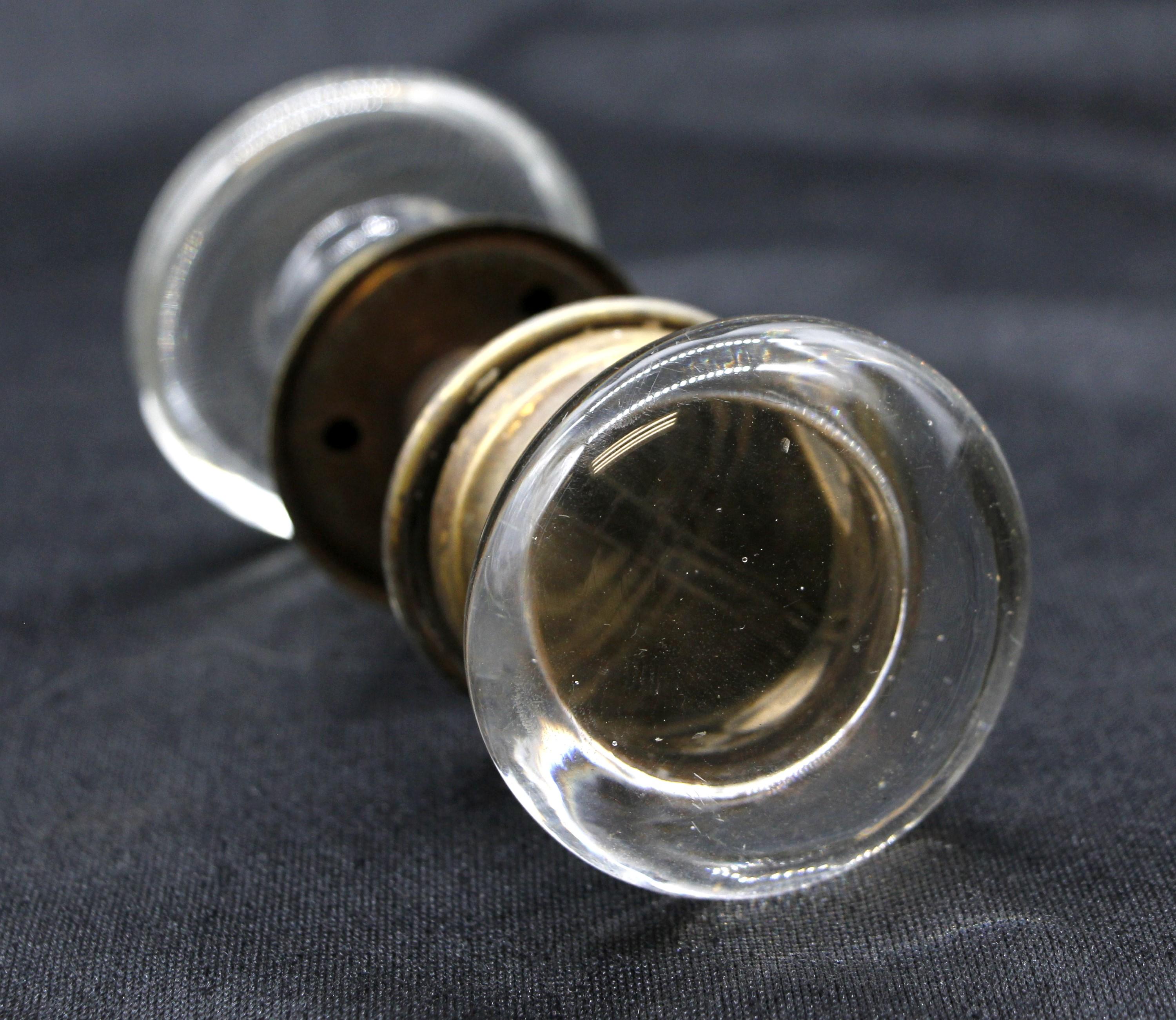 Early 20th century clear glass antique door knobs with a center apostolic cross, thin brass rosettes and spindle. Each set consists of two door knobs, two rosettes and a matching spindle. Small quantity available at time of posting. Priced each.