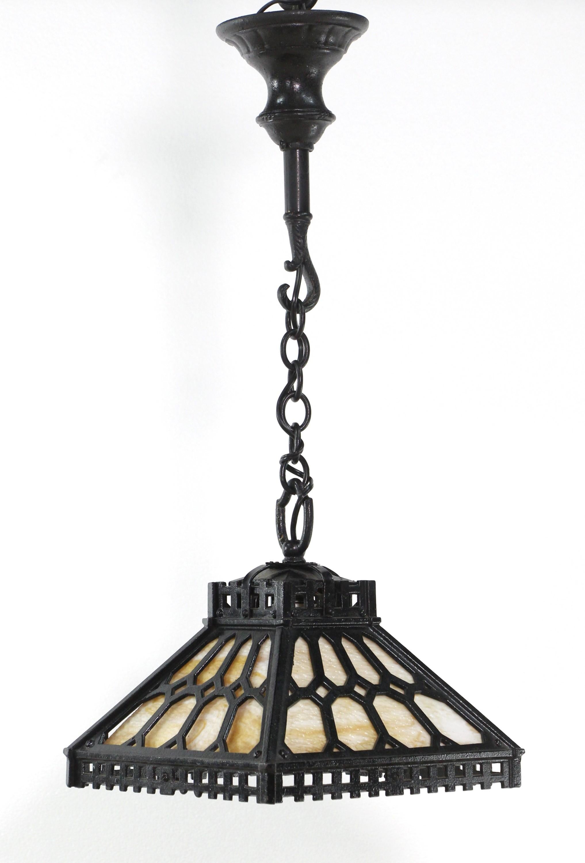 Early 20th century black iron pendant light featuring light colored swirled stained slag glass panels. Intricate details. Adjustable height.