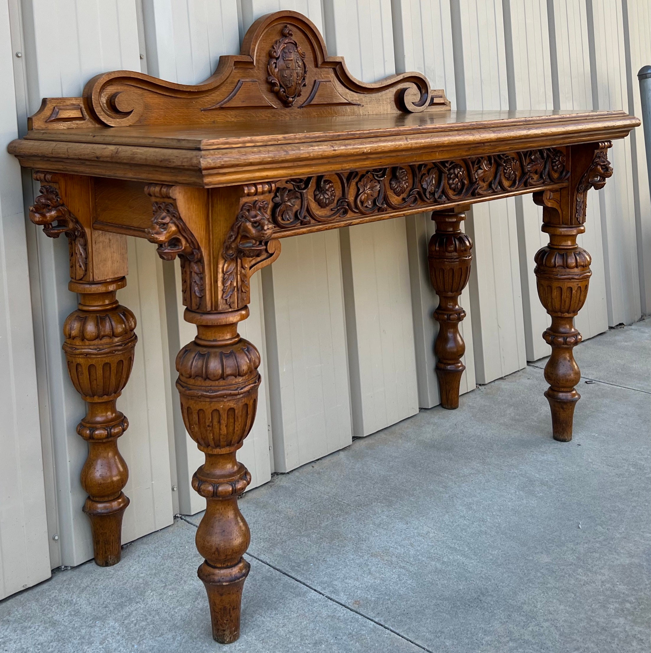 Love this piece! This is an early 20th century heavily carved oak British colonial server. The apron has stand out detail with it’s plethera of carved lion busts. The backboard features a carved crest. It is 36 inches from thr floor to the serving