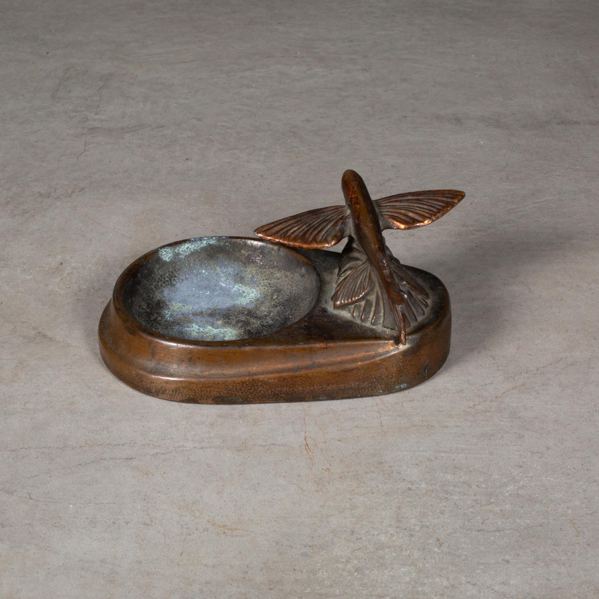 ABOUT

An early 20th century bronze plated Flying Fish coin dish.

    CREATOR Unknown.
    DATE OF MANUFACTURE c.1930-1940.
    MATERIALS AND TECHNIQUES Bronze.
    CONDITION Good. Wear consistent with age and use.
    DIMENSIONS H 2 in. W 5 in. D