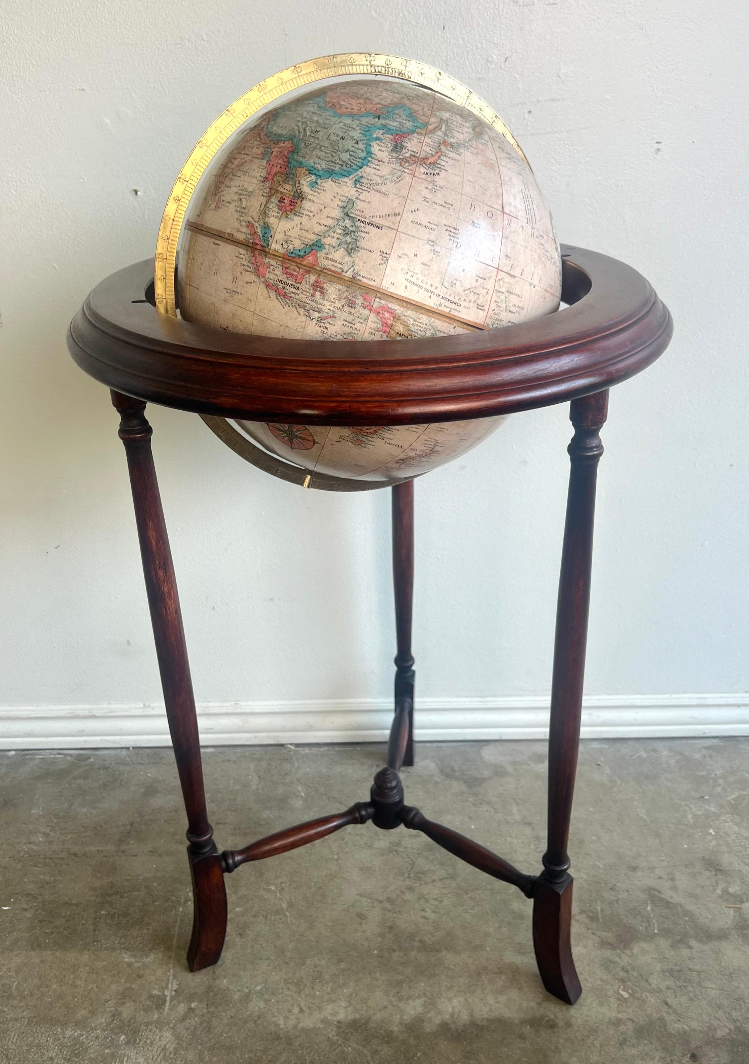 Globe terrestre vintage monté sur un socle en bois d'acajou avec trois pieds élégamment tournés.  Un anneau méridien de couleur laiton entoure le globe, ajoutant à son esthétique antique.  Le support en bois est doté d'un cadre circulaire qui