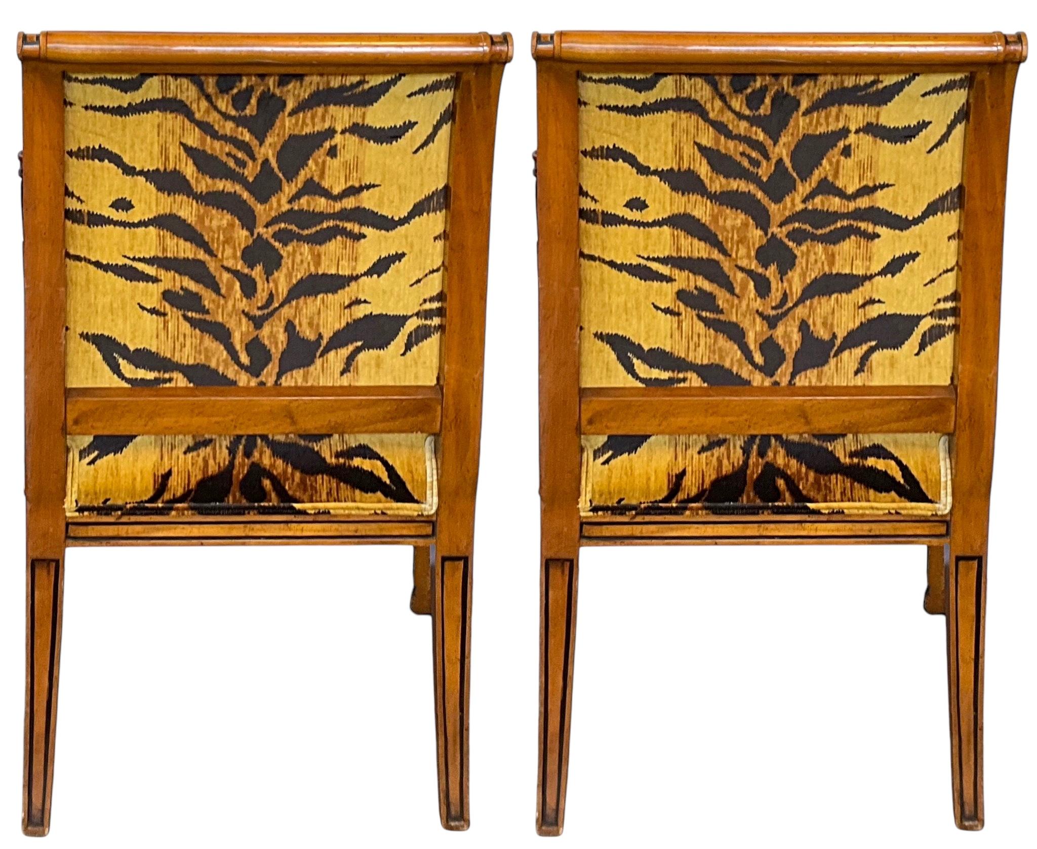 These are striking! This is a pair of carved bergere chairs newly upholstered in a tiger velvet. They have Egyptian Revival styling with the carved sphinx arm supports and gilded paws. The chairs also have a painted ebony pinstripe. They are