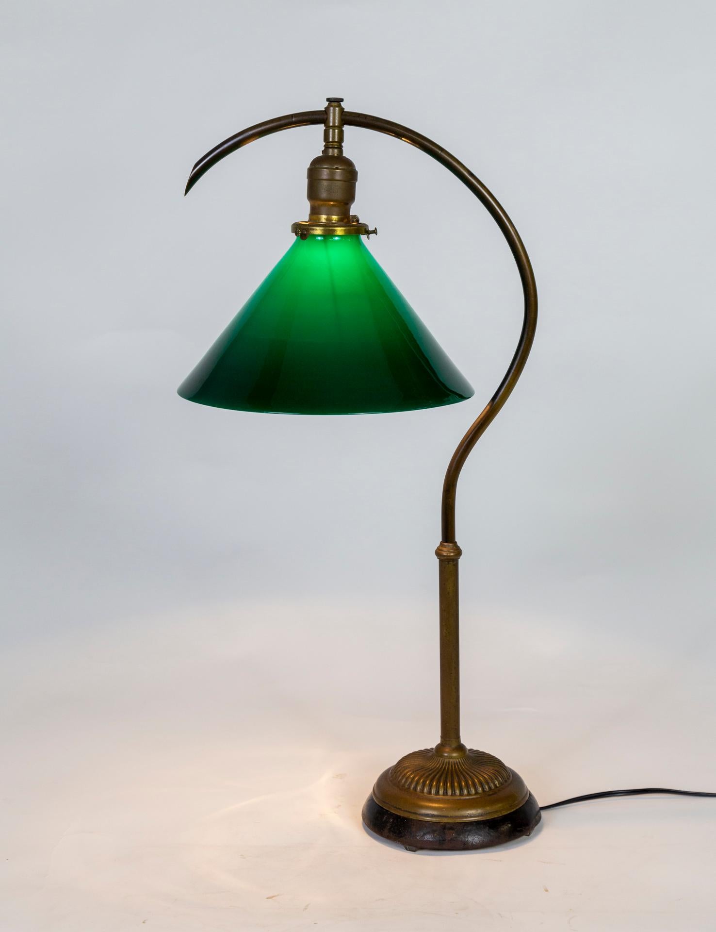 An adjustable Banker's lamp with a cone shaped, green shade fabricated by Faries Lamp Co. The elegant, curved pipe stem has telescoping height adjustment and the shade holder, with detailed set screws, swivels direction. The gadrooned brass base