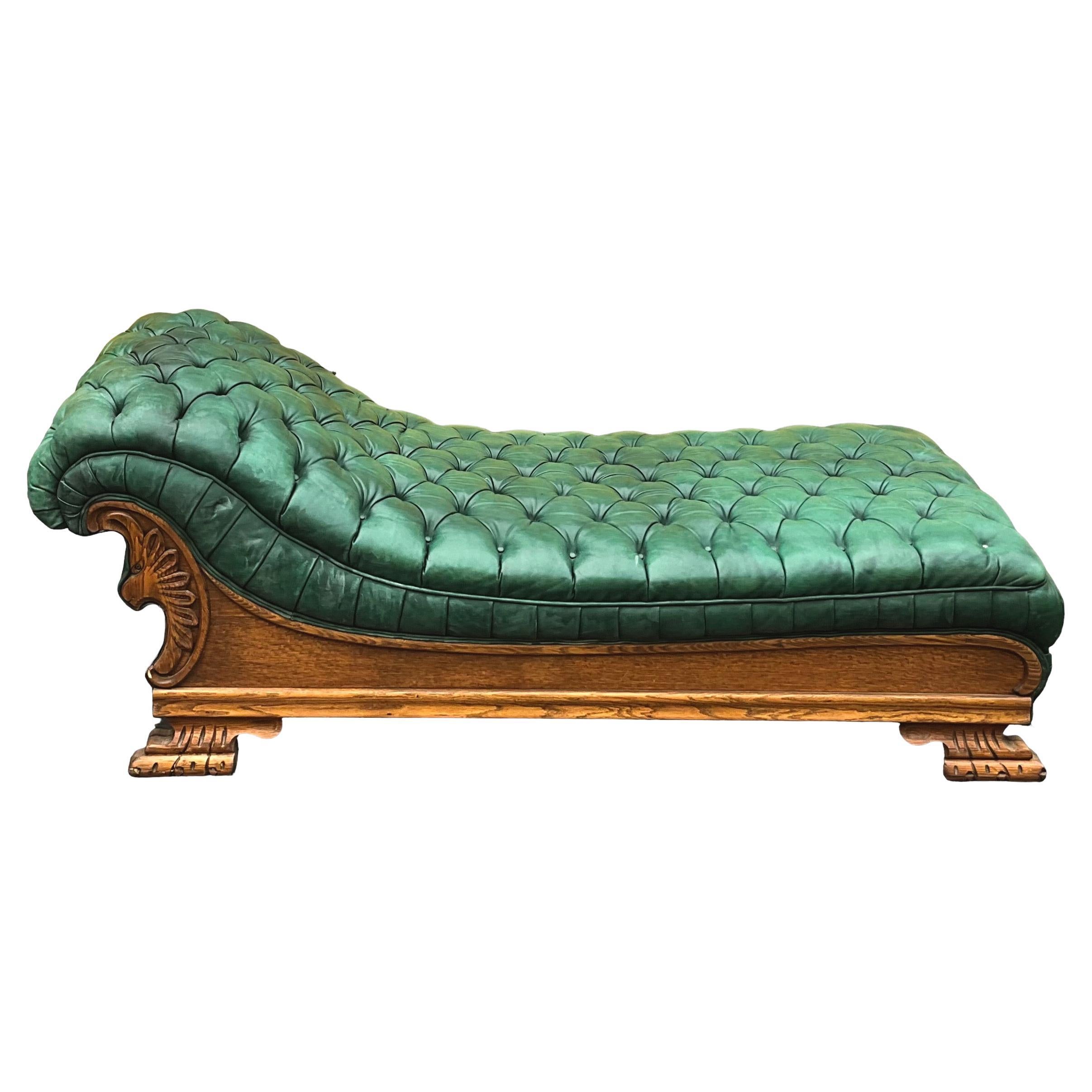 This is an early 20th century Empire style green tufted leather chaise. It was manufactured in New York in approximately 1920 by Kroehler Manufacturing Company. It is marked. The oak frame depicts a Neo-classical style carved griffin. It is