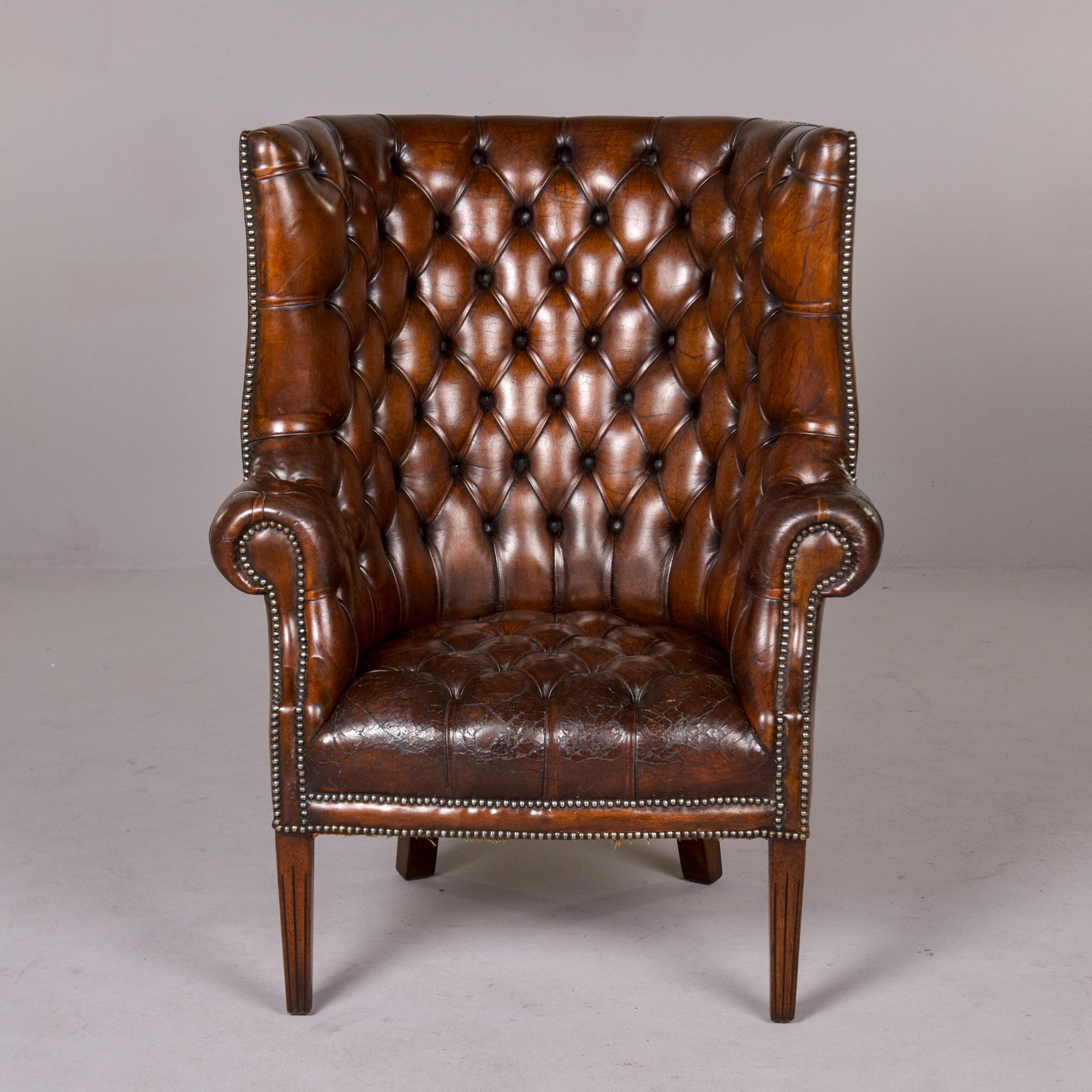 Found in England, this leather wing back library chair dates from the 1910 - 1920s. Tall seat back, wings and seat are upholstered in original button-tufted leather with brass nail head trim. Legs appear to be dark stained walnut. Front legs are