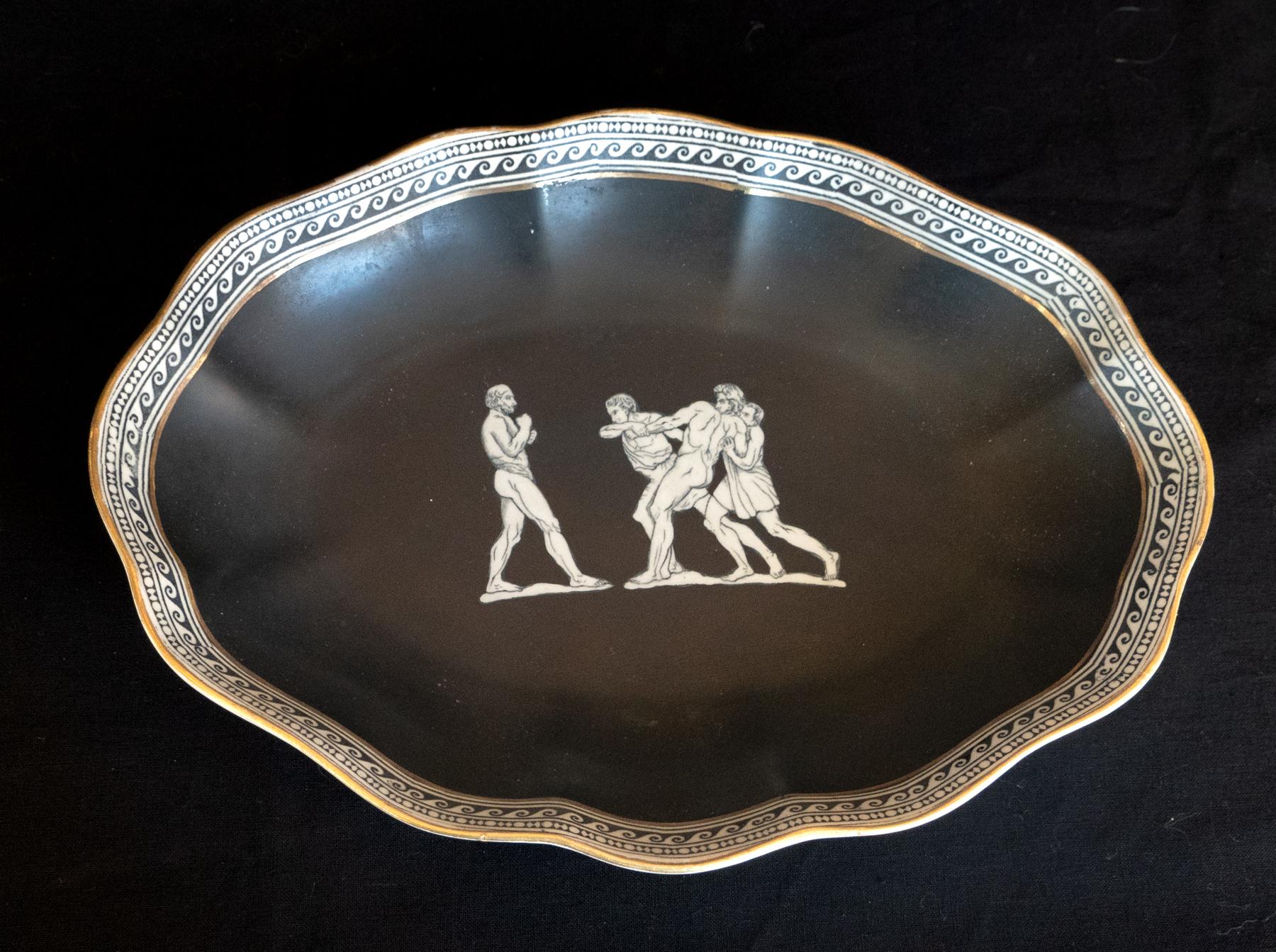 Early 20th century english foilate oval form platter w/ Classic Greco Roman Wrestlers.Gold gilt on the rim with an intricate transferrer border. Black ground with white figure drawn in a combative pose. Decorative. minor losses to the gold gilt