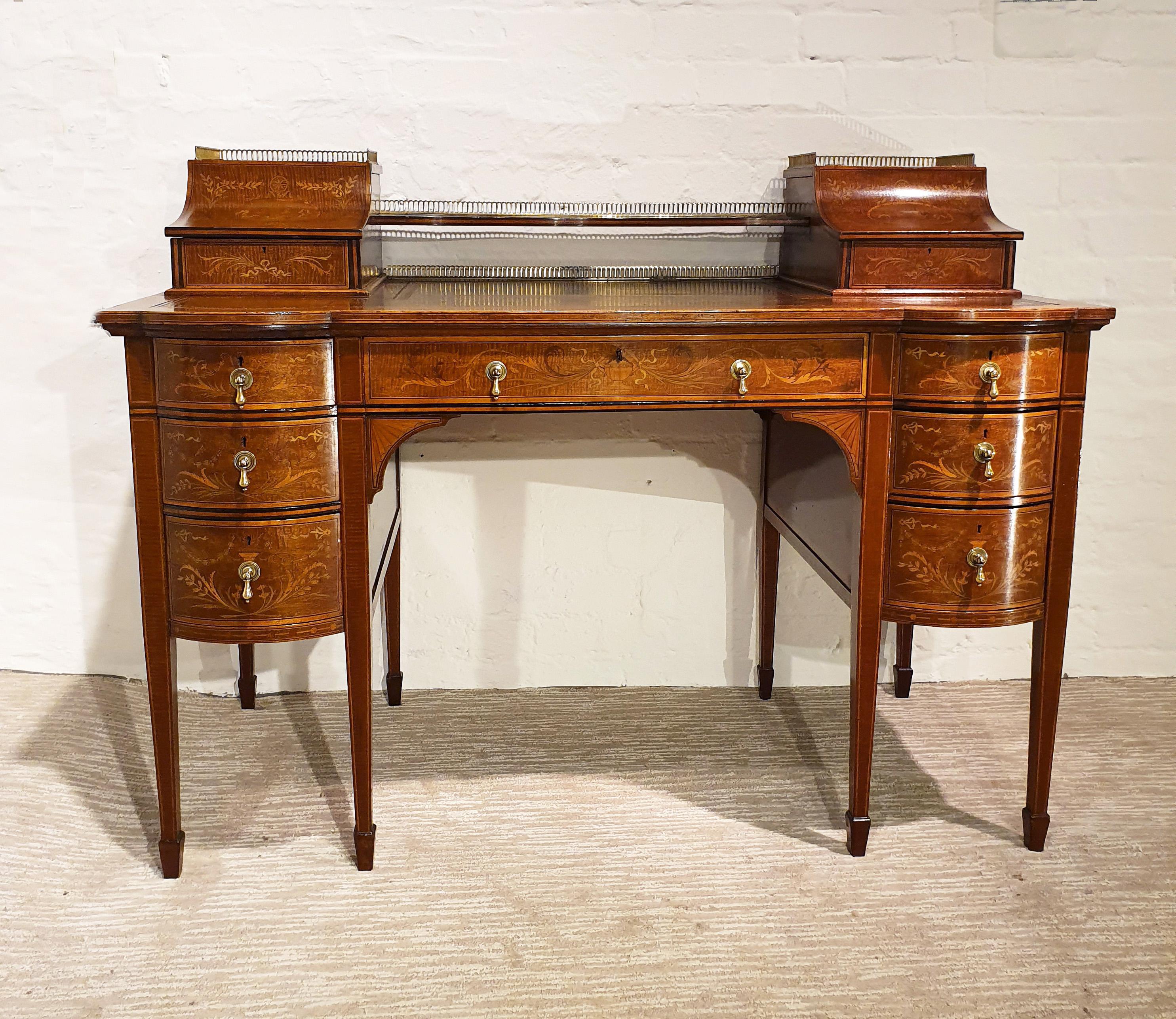 This good looking and very detailed early 20th century English mahogany writing desk is a Sheraton Revival desk, inlaid with ornate satinwood detailing of scrolls, bows and ferns as well as stringing detail along the squared tapered legs. The desk