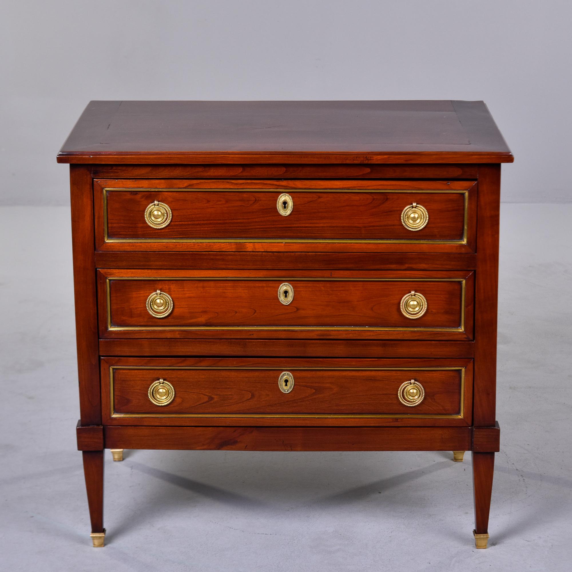 Found in England, this three drawer cherry chest dates from the 1920s. This handsome chest is a versatile size and could be used next to a sofa or bed. Drawers feature dovetail construction, brass-trimmed fronts, brass ring-pull hardware and