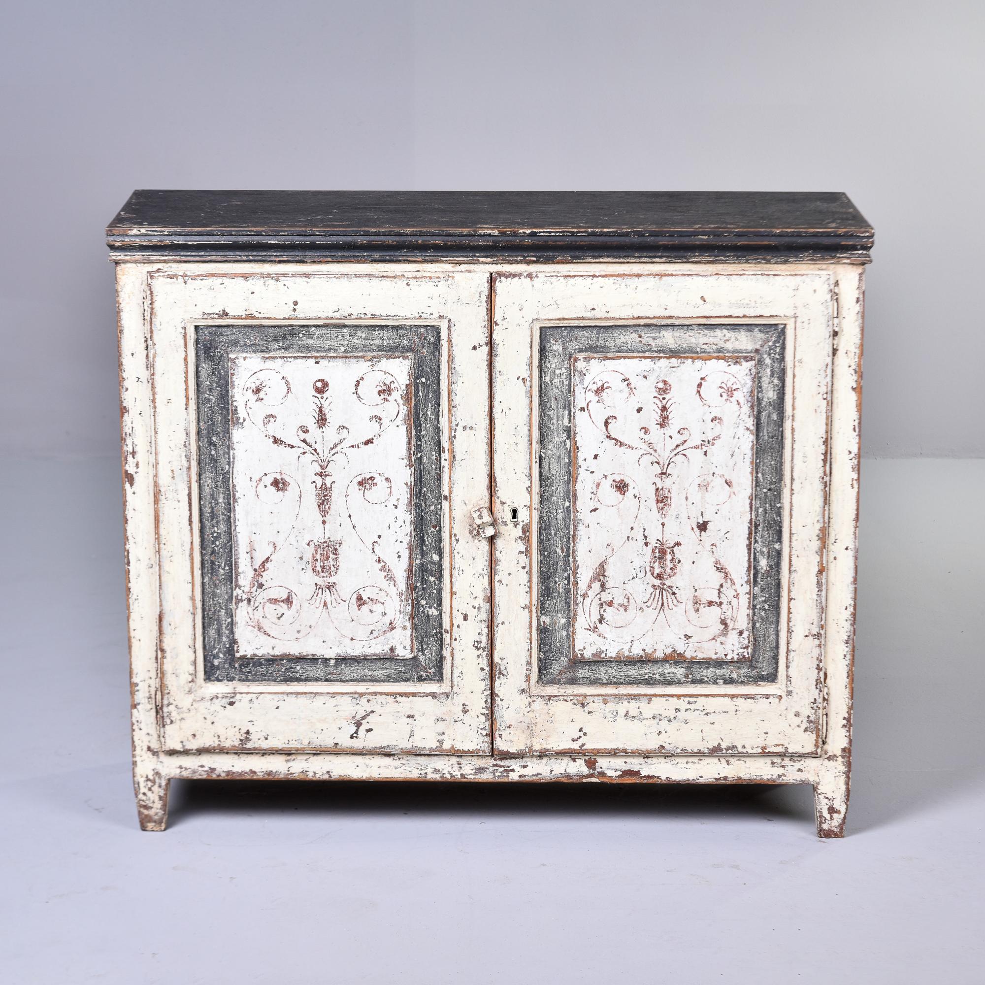 Found in England, this two door painted wood cabinet dates from the 1930s. Painted finish features a slate gray colored top with antique white on the sides and fronts. Door fronts have a contrasting gray border and white centers with decorative