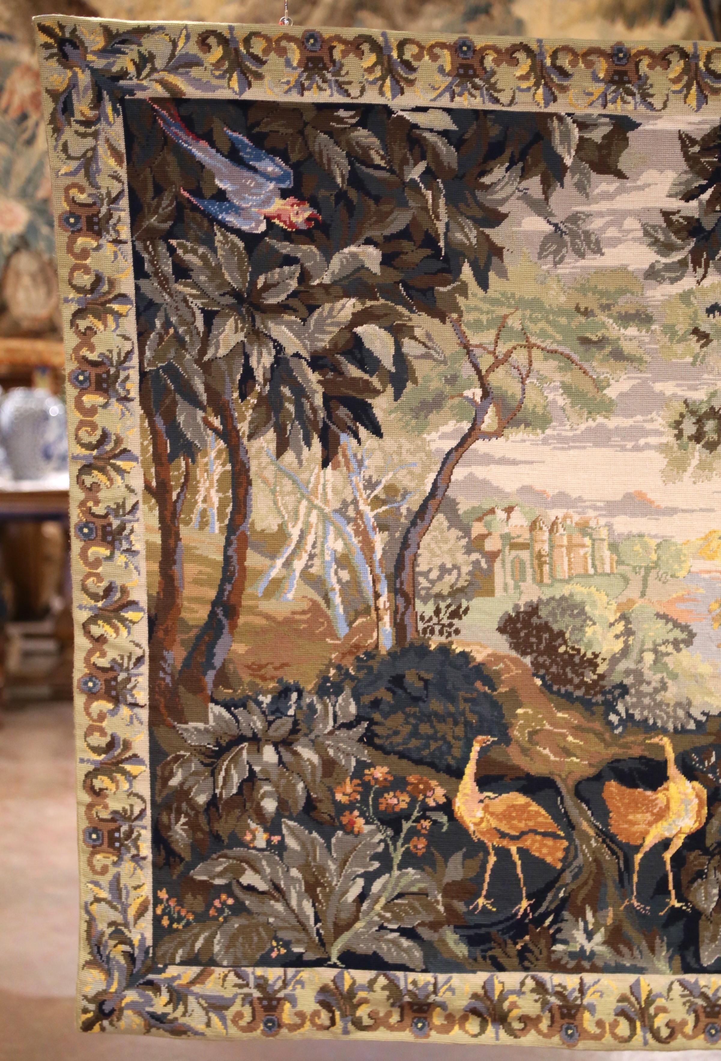 Porta eleganza e fascino pastorale nel tuo spazio con questo raffinato arazzo Aubusson francese. Tessuta a mano all'inizio del XX secolo, la composizione raffigura un sereno paesaggio boschivo animato da un fogliame lussureggiante, uccelli esotici e