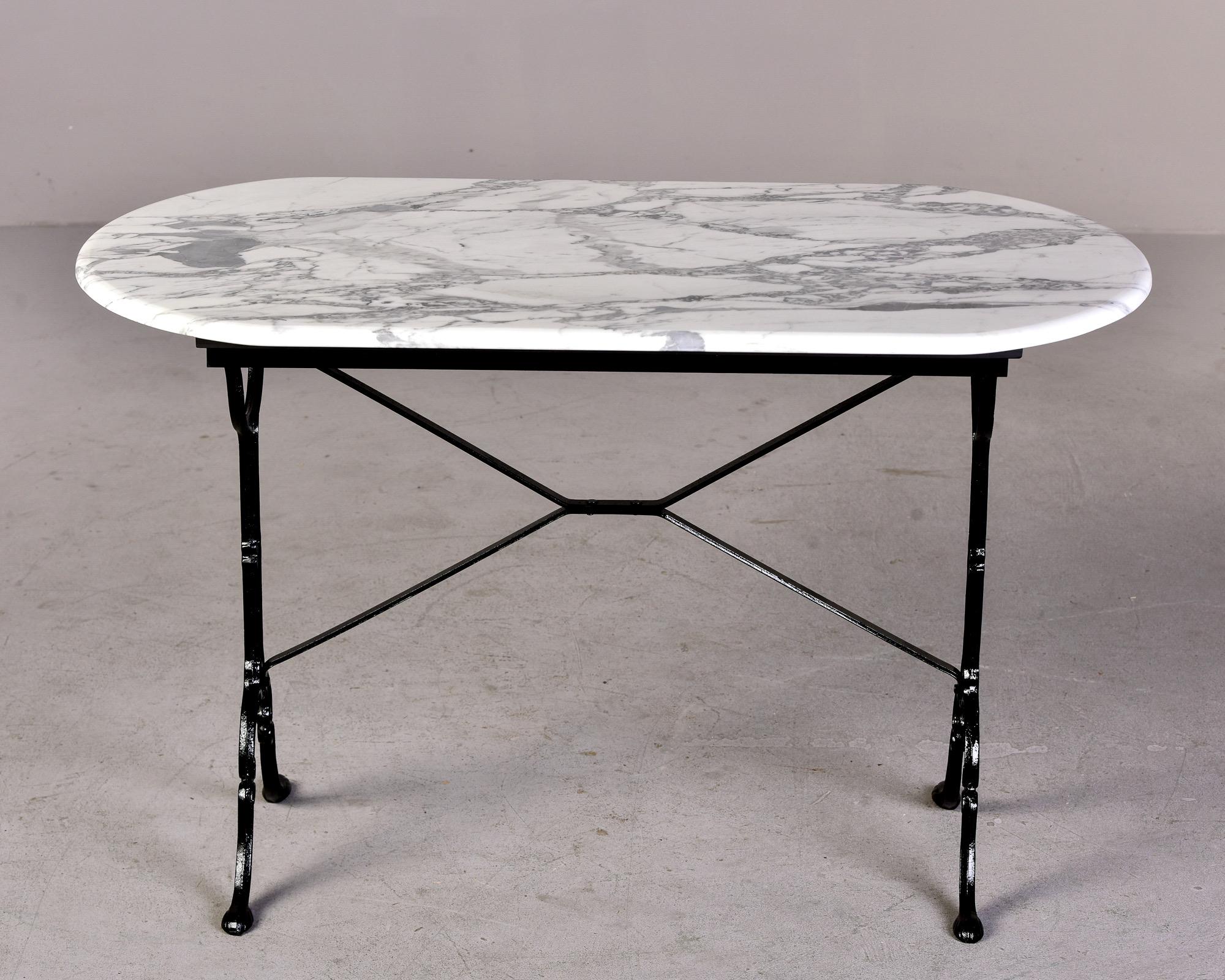 Circa 1920s French iron and marble bistro table. Iron base with black painted finish and new oval carrara marble top. Unknown maker. 