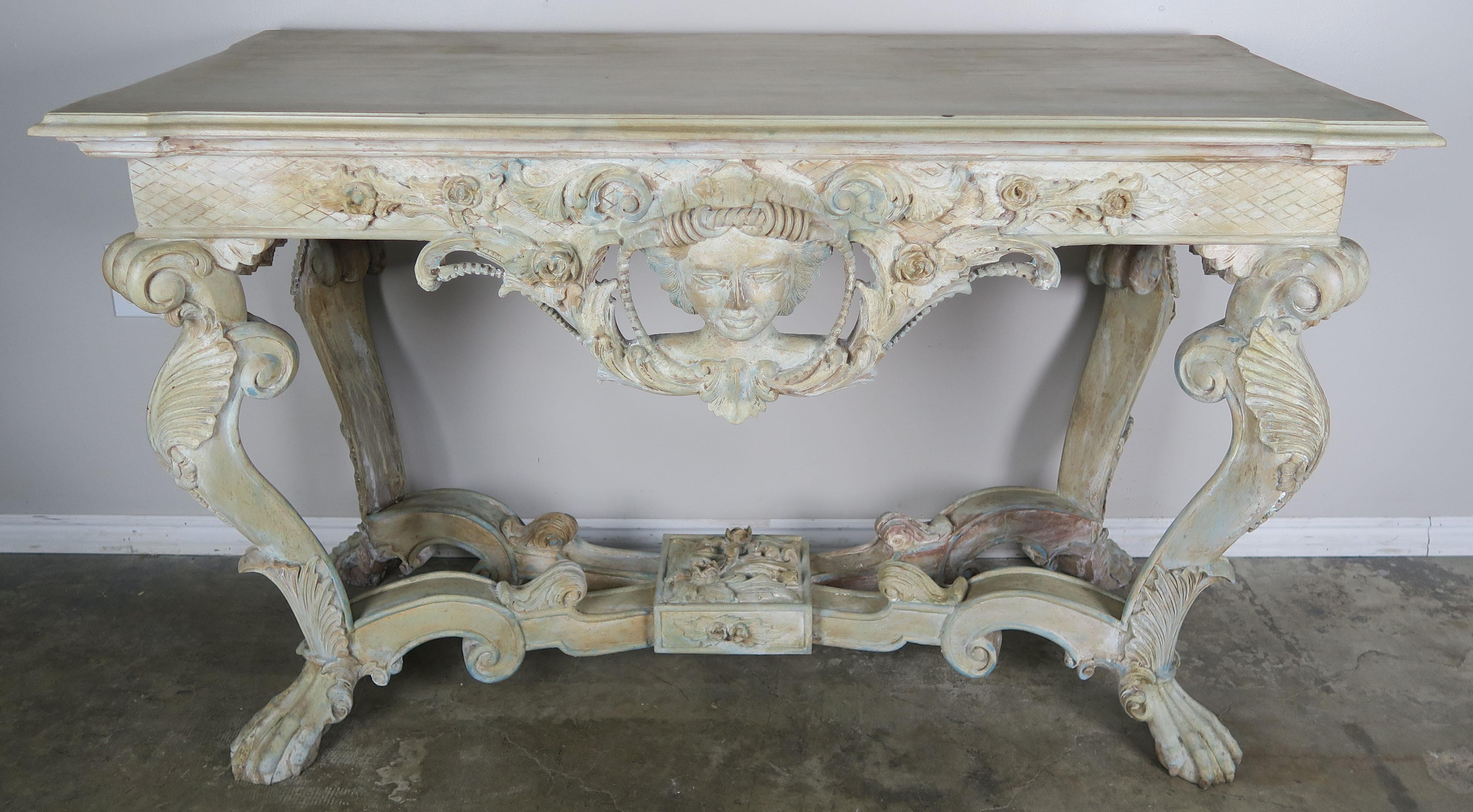 Early 1900s French carved softly hand painted console table with intricate carved detail of woman's face, shells, acanthus leaves, flowers, scrolls, and so much more. The finish is painted in soft muted colors that include a cream base with accents