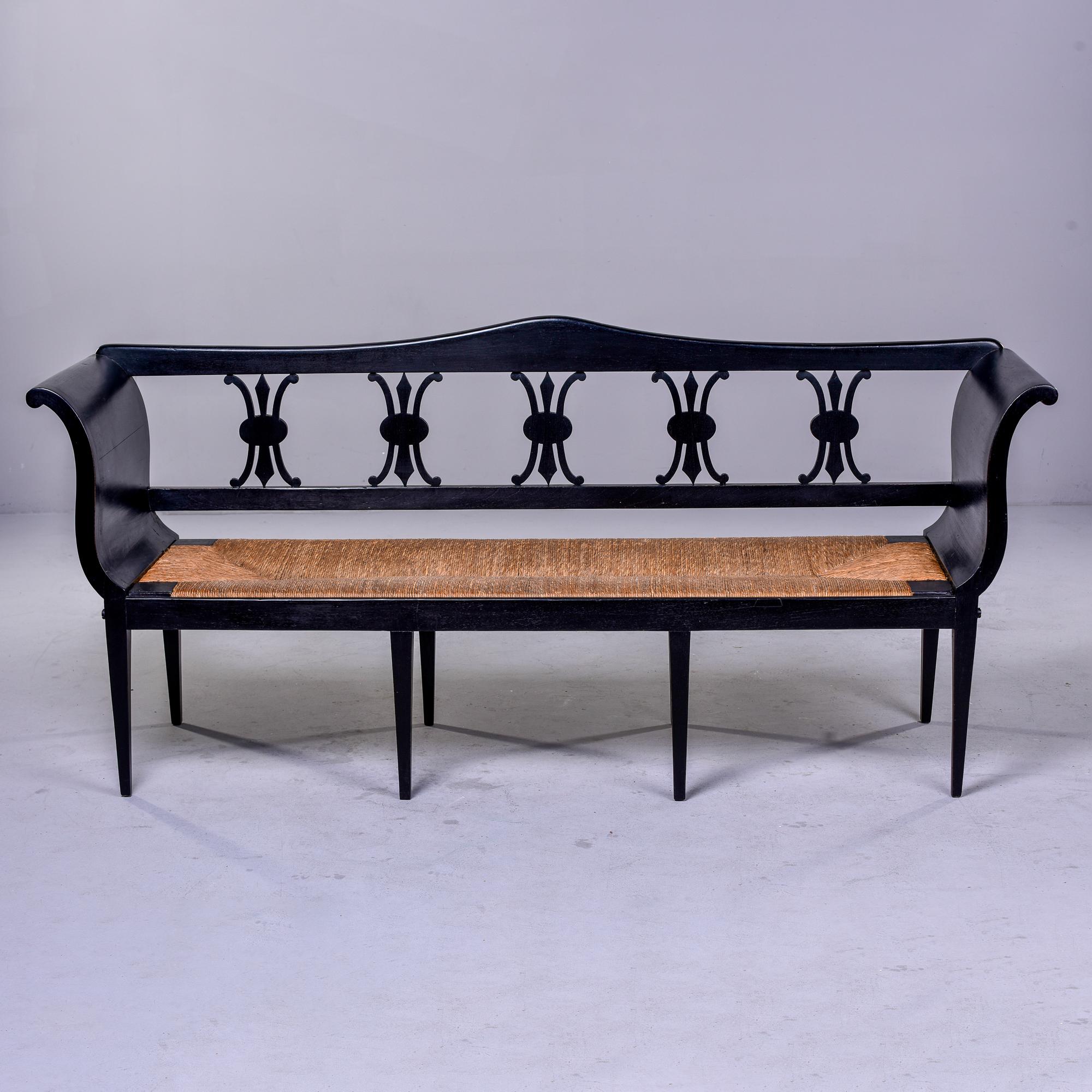 Circa 1920s French bench has eight legs, high curved sides, decorative carved backrest and woven rush seat. New black ebonised finish. Unknown maker. Very good antique condition with minor scattered wear to surfaces. 

Arm Height: 32.5” Seat
