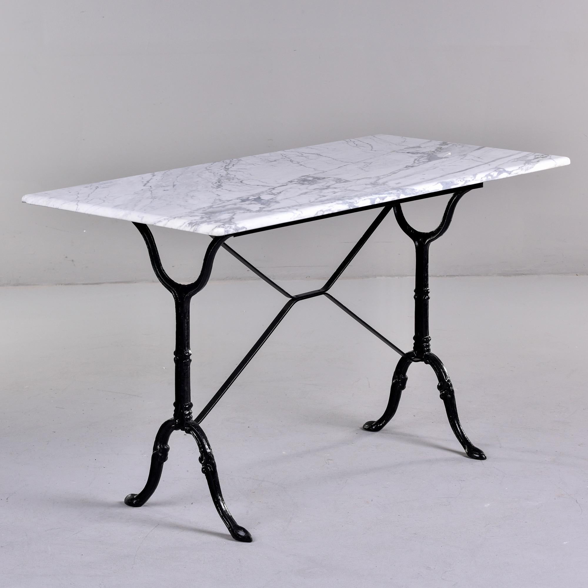 Circa 1920s French bistro table features a classically styled iron base with black painted finish and a rectangular white carrara marble top. Top has finished and polished edges all around. One corner has a small flake on underside - see detail