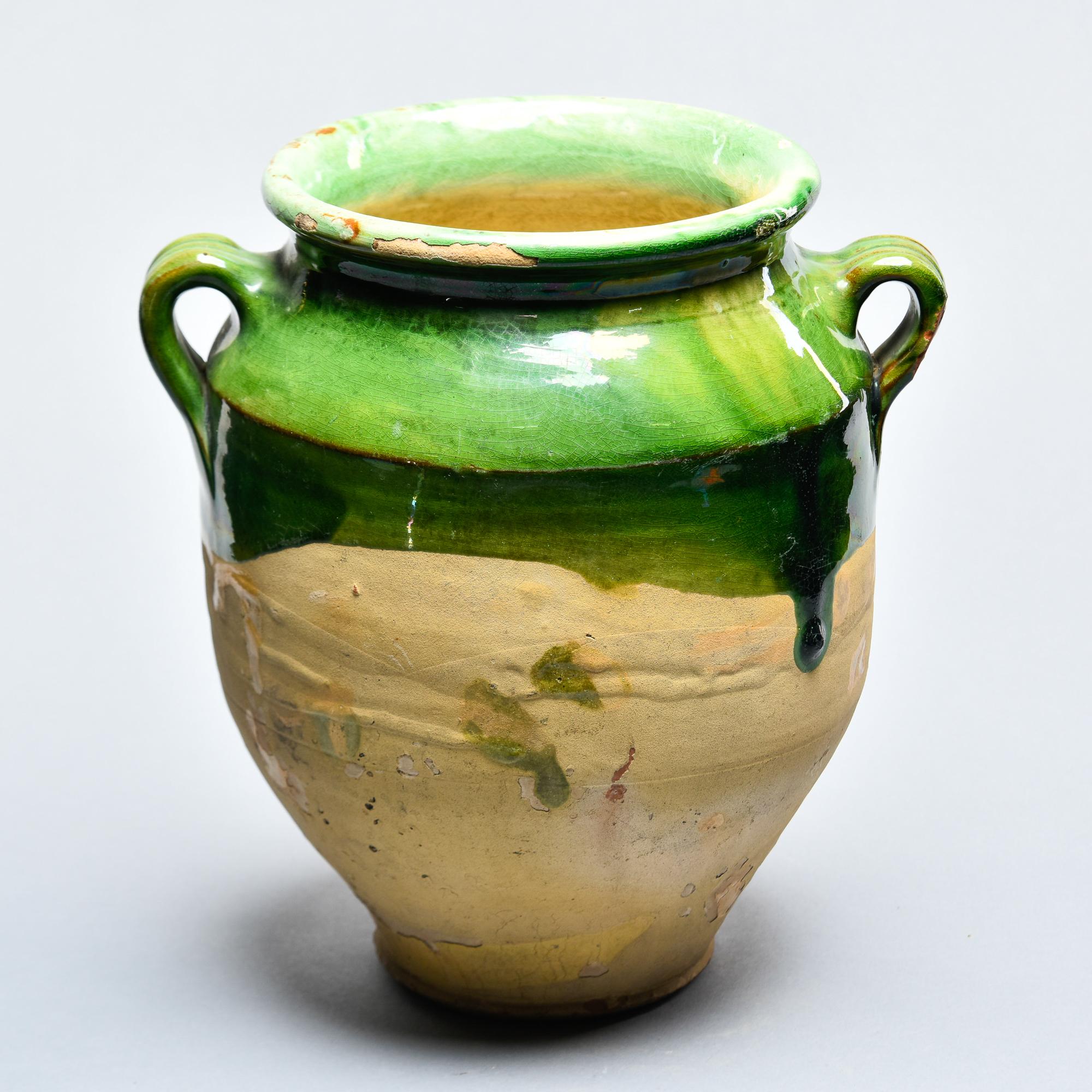 Found in France, this French confit jar dates from approximately 1915. This piece stands 11” high and has the traditional form with a wide vessel body and two handles on the sides with a green colored glaze on the outside top half and fully glazed