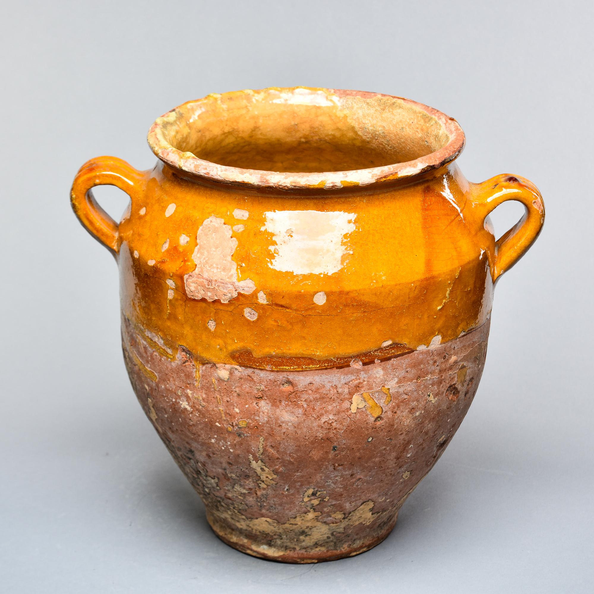 Found in France, this French confit jar dates from approximately 1915. This piece stands 11.75” high and has the traditional form with a wide vessel body and two handles on the sides with a dark mustard-colored glaze on the outside top half and