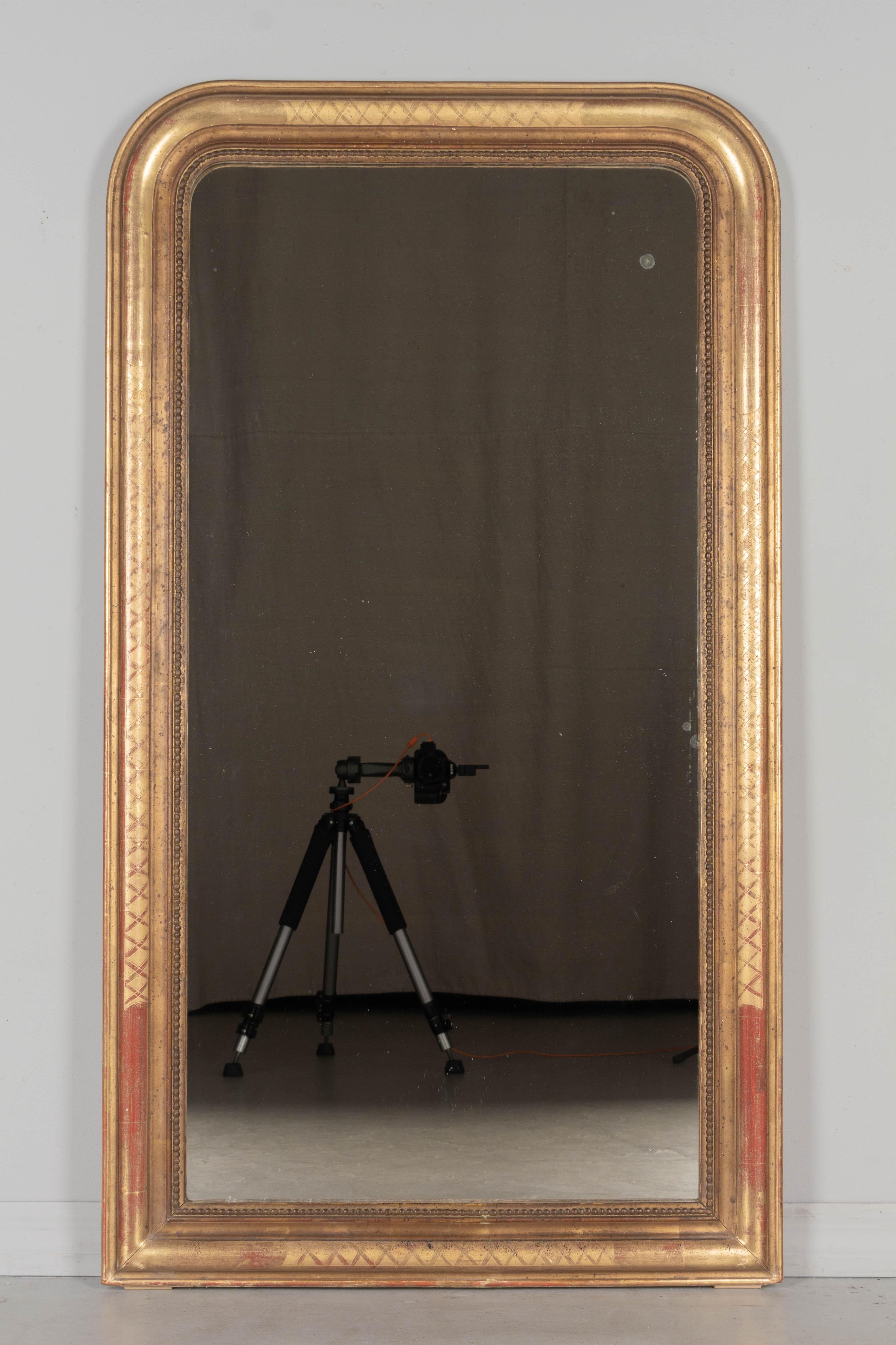 An early 20th century French Louis Philippe style gilded mirror with curved top corners, incised decoration and inner bead border. Warm gilt finish with red under rub exposed. Original mirror. Frame has been minimally restored at bottom corners.