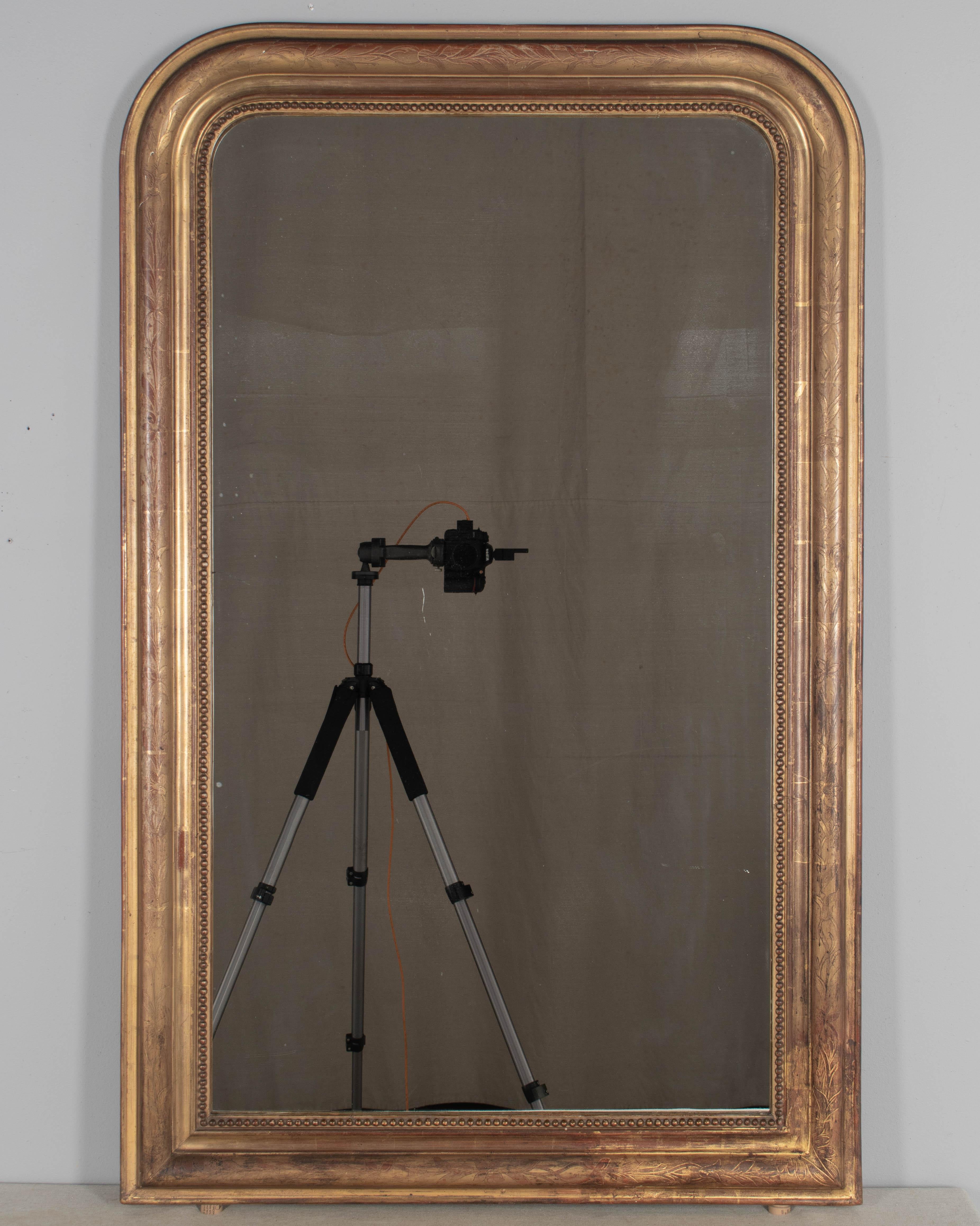 An early 20th century French Louis Philippe style gilded mirror with curved top corners, incised floral decoration and inner bead border. Warm gilt finish with red under rub exposed. Original mirror with slight fogging. Very good quality and
