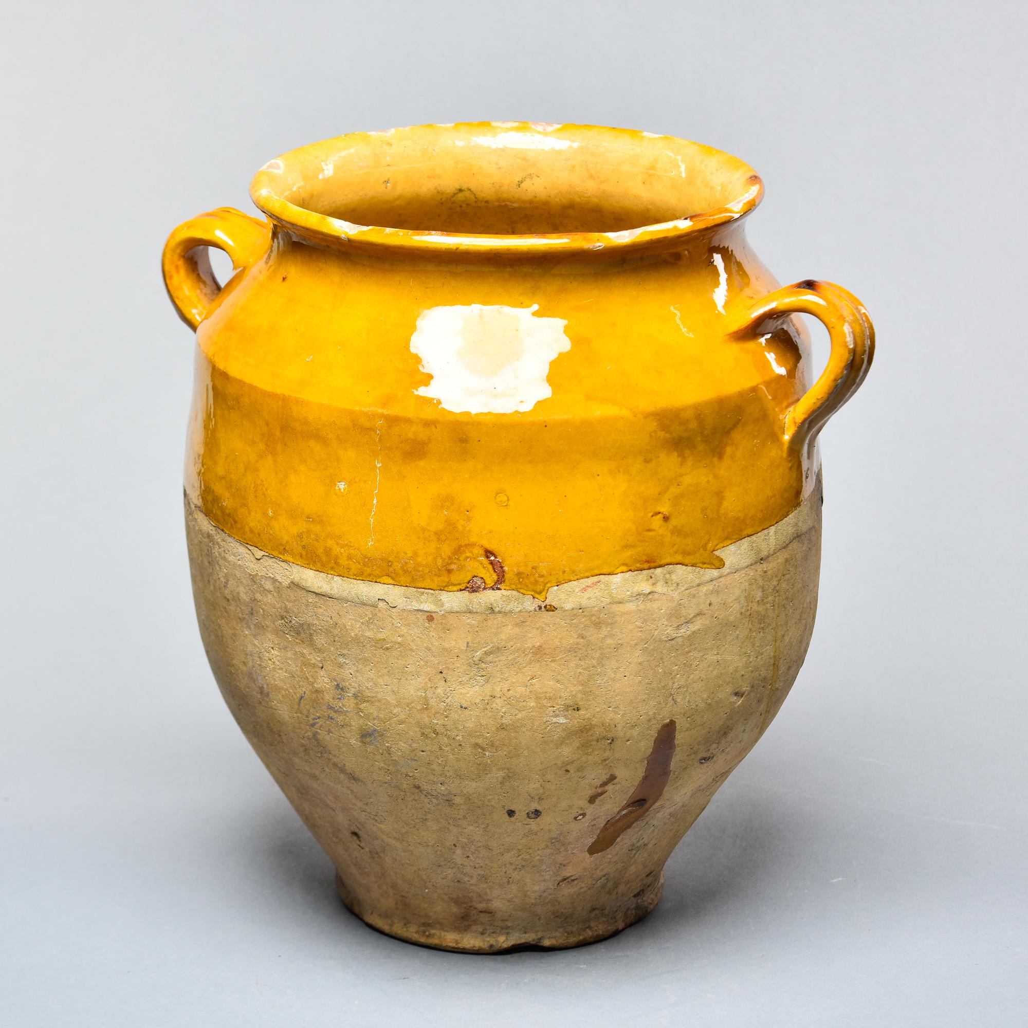Found in France, this French confit jar dates from approximately 1915. This piece stands 11.5” high and has the traditional form with a wide vessel body and two handles on the sides with a mustard-colored glaze on the outside top half and fully