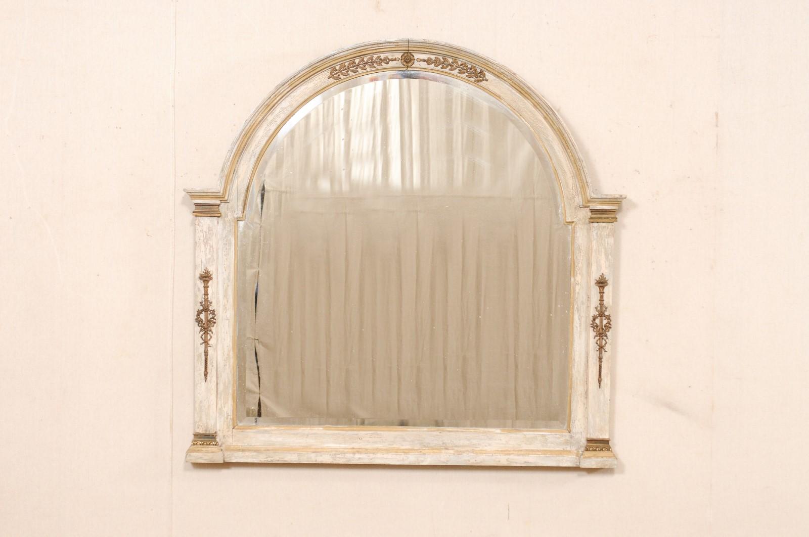 A French carved and painted wood mirror from the early 20th century. This antique mirror from France has a frame comprised of a wonderful arch-shaped top, which terminates at the shoulders onto two column style sides, which flank the mirror at