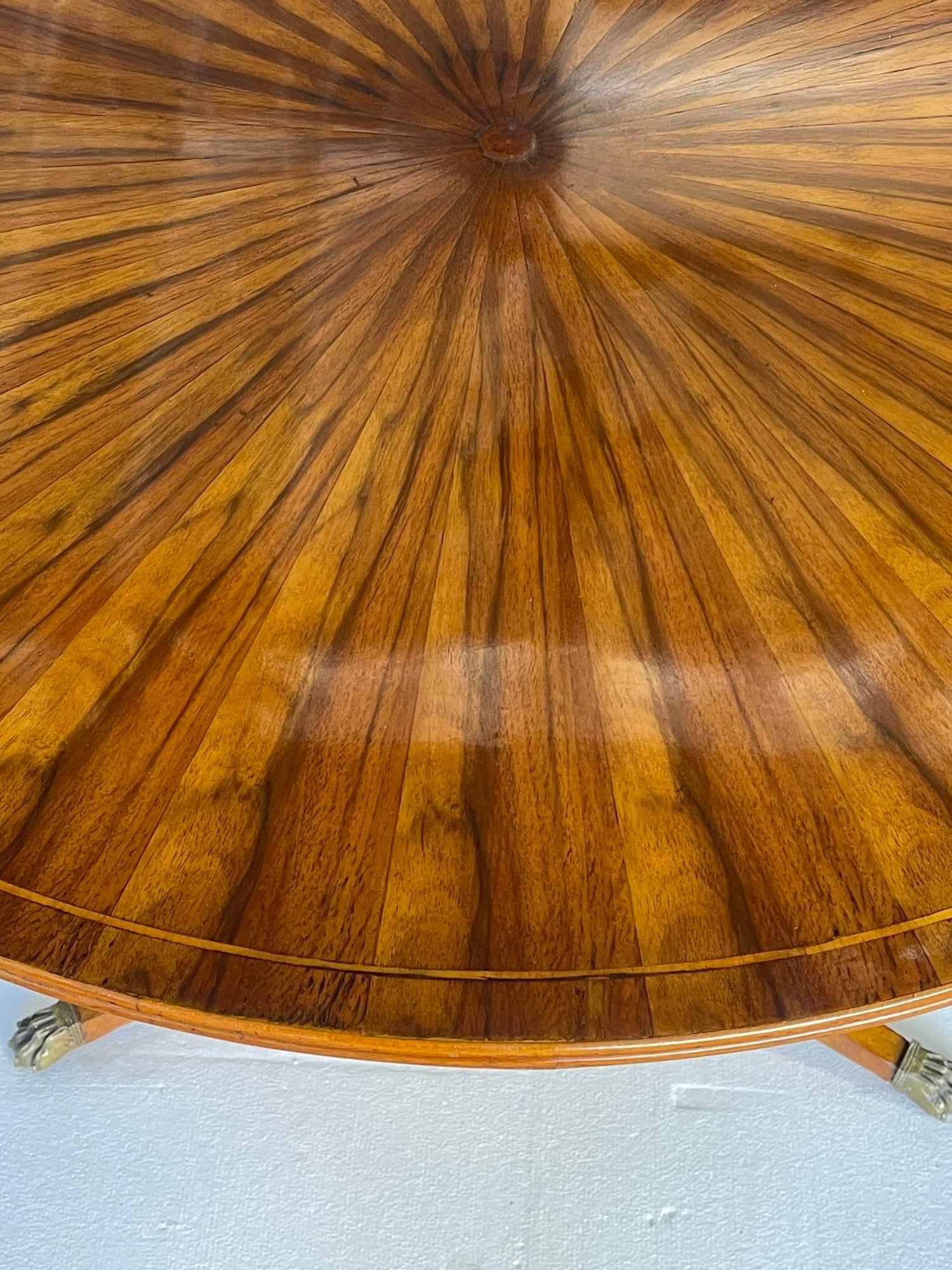 This exquisite early 20th-century French Regency-style round table showcases a stunning sunburst inlay on its maple and walnut top, bringing warmth and sophistication to any room. Expertly crafted in France, the table is elevated by a beautifully