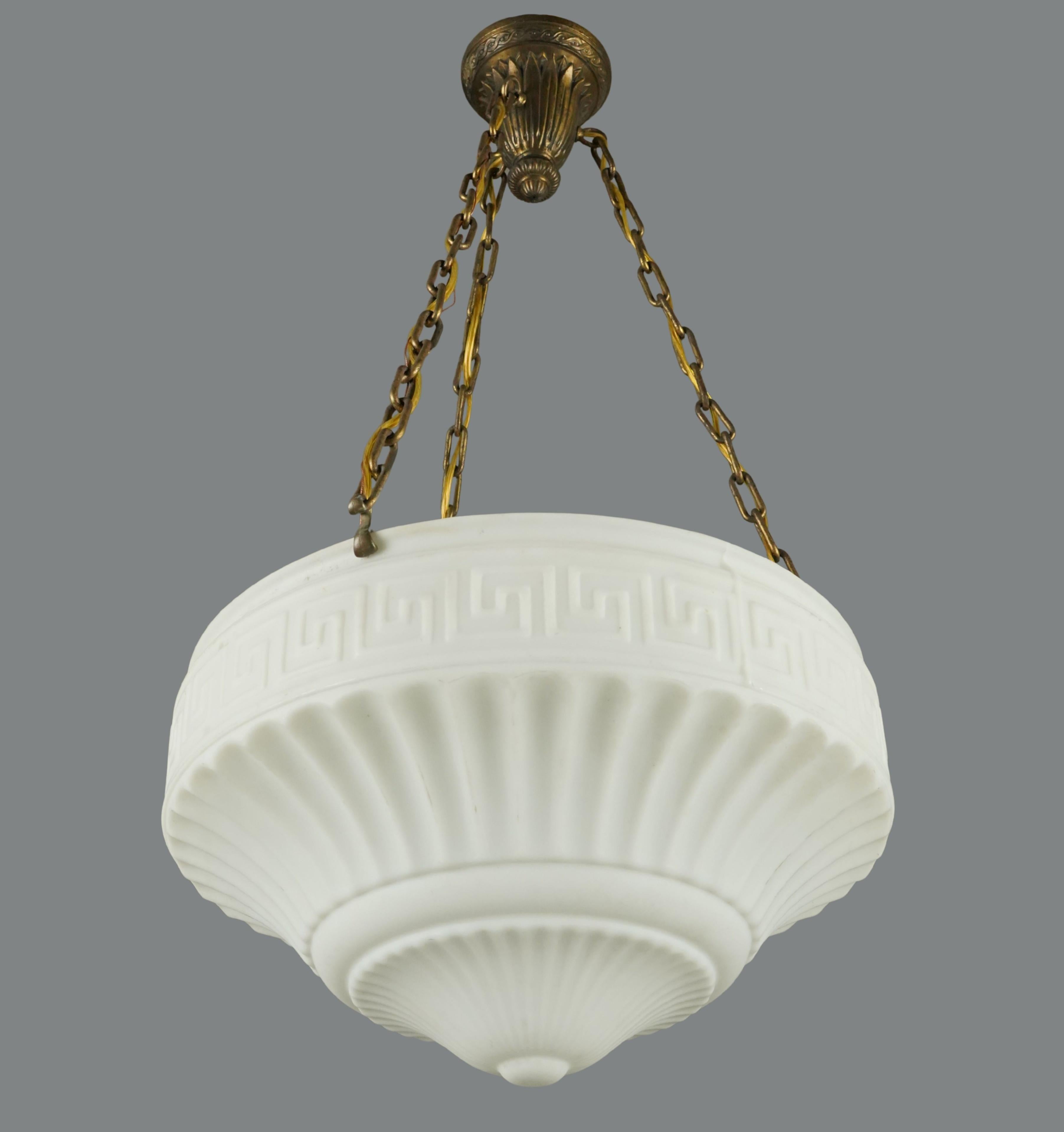 Early 20th Century pendant light featuring a white milk glass dish shade with a fluted and Greek key design, a brass finish steel chain, and a bronze canopy. This requires three standard Edison style medium base bulbs. Cleaned and restored. Good