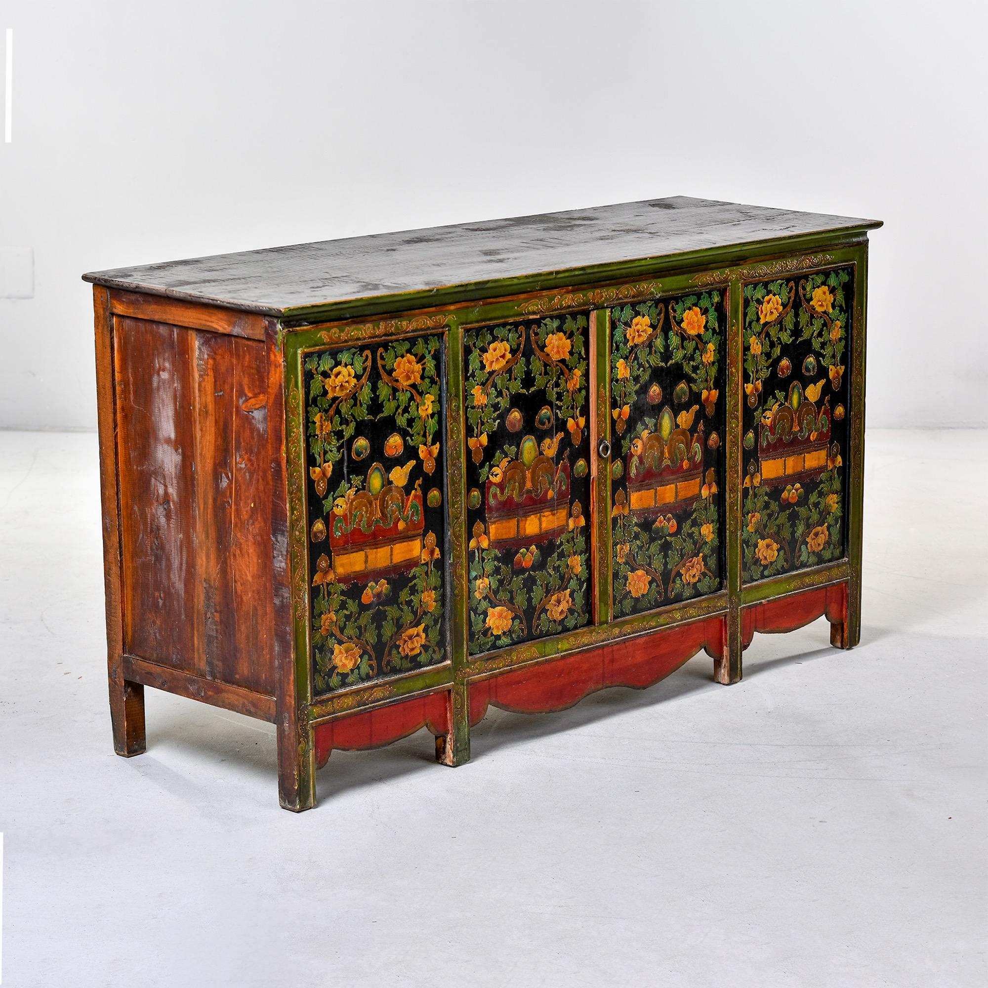 Circa 1910 Tibetan cabinet has four hand painted panels with a floral design in green, black, and gold with red accents. Scalloped red apron. Two center doors open to storage compartment. Mortis and tenon construction. Unknown maker.