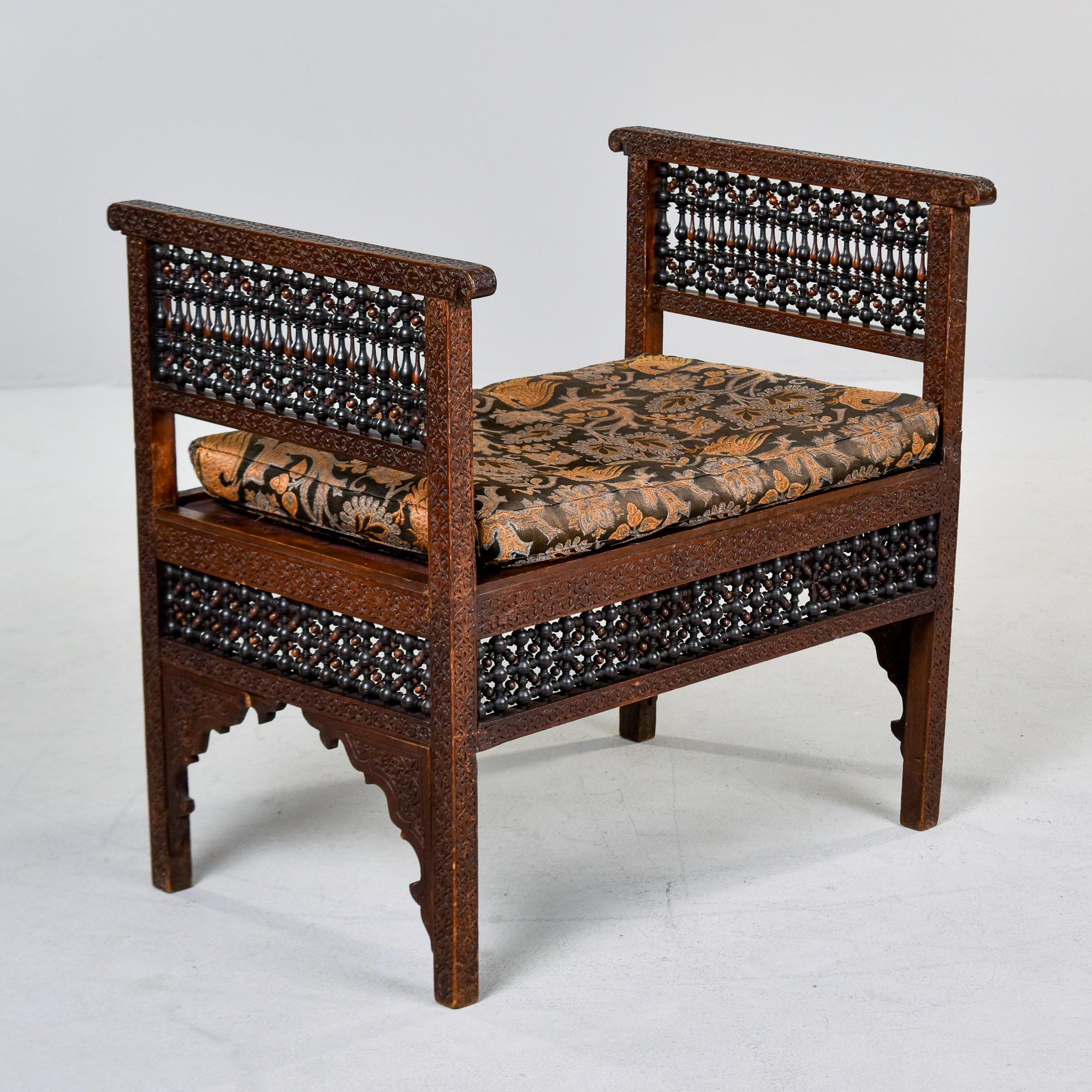 Found in Turkey, this heavily carved bench with cushion dates from the 1910s. Dark stained wood frame - we believe this is teak but cannot be sure - has intricate, highly carved detail on the high sides and apron. Moorish style arched opening on