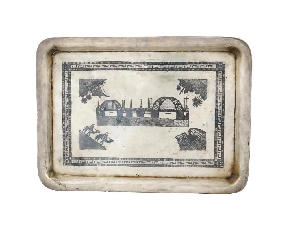 A large early 20th-century Iraqi silver serving tray. Rectangular shape, elevated rims. The center of the piece is decorated with niello images, sailing ship, camel riders, mosque ruins, palm trees, a bridge. Total Weight: 1100 grams. Oriental