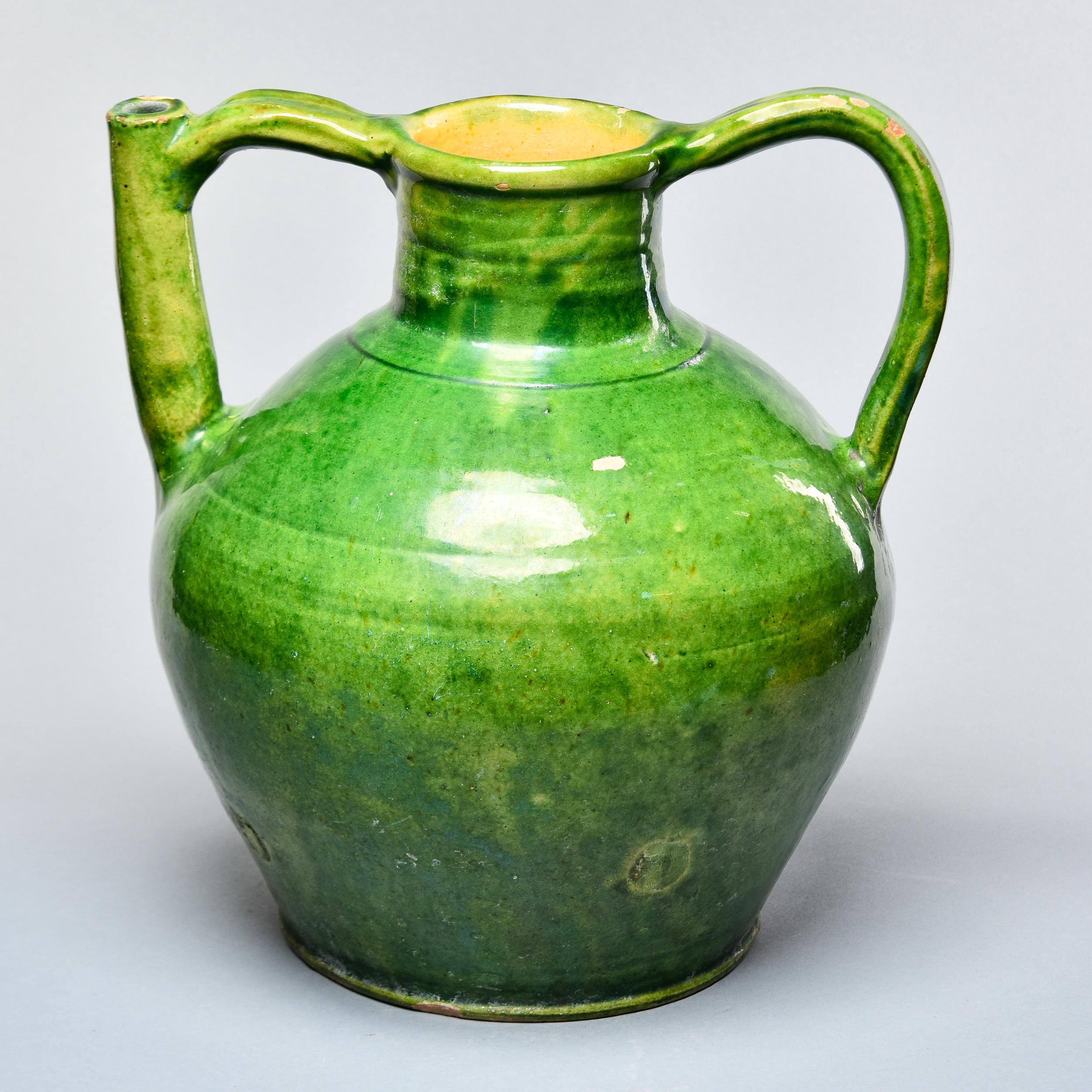 Found in France, this French glazed ceramic water jar dates from approximately 1915. This piece stands 13.5” high and has a wide vessel body, narrow neck and two handles on the sides, one of which also functions as a pouring spout.  The piece has a
