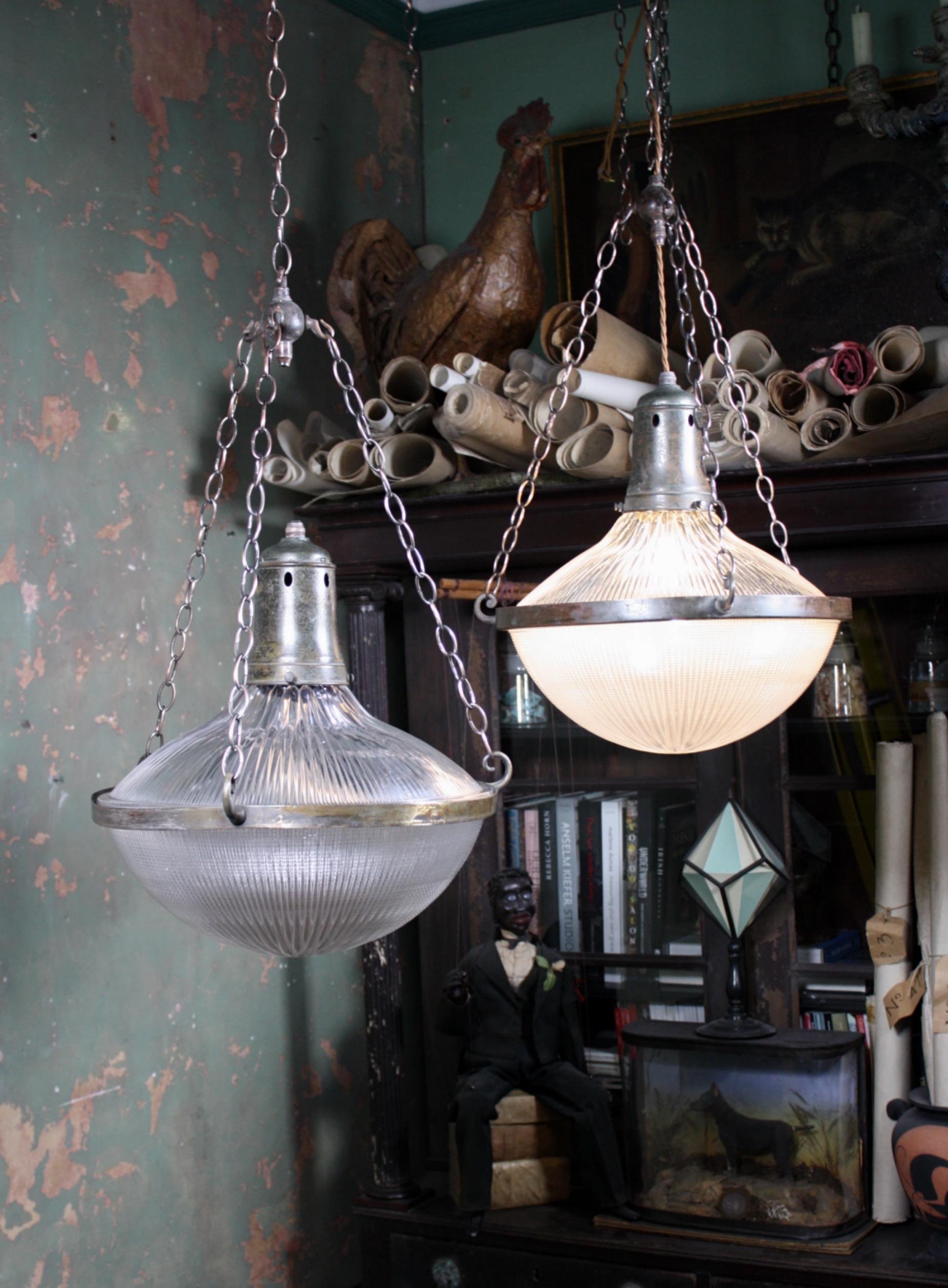 A rare pair of large two part Holophane stiletto pendants, two sections of prismatic cut glass sit within a central band. Three chains terminate to a four way chandelier hook, each light has its original Holophane brass gallery (stamped). 

All