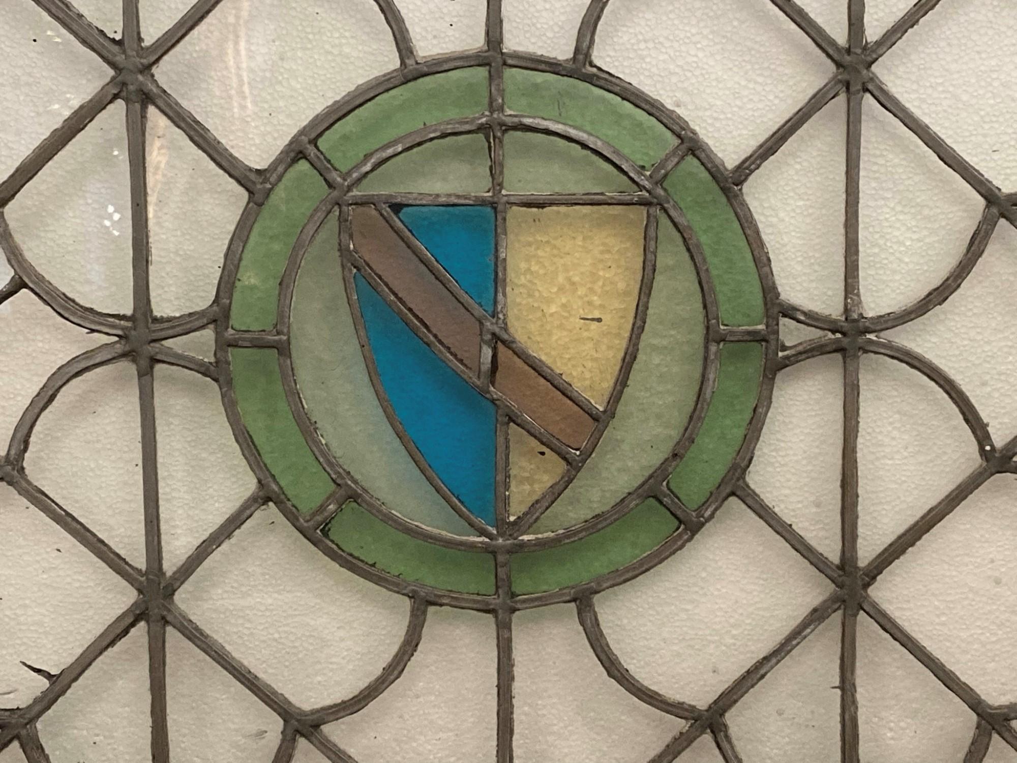Originally a pivoted window, this wood framed leaded glass window can either have the present frame trimmed down or be reinstalled in anew frame. This features a stained glass shield motif in the center done in rich colors. Clear glass background in