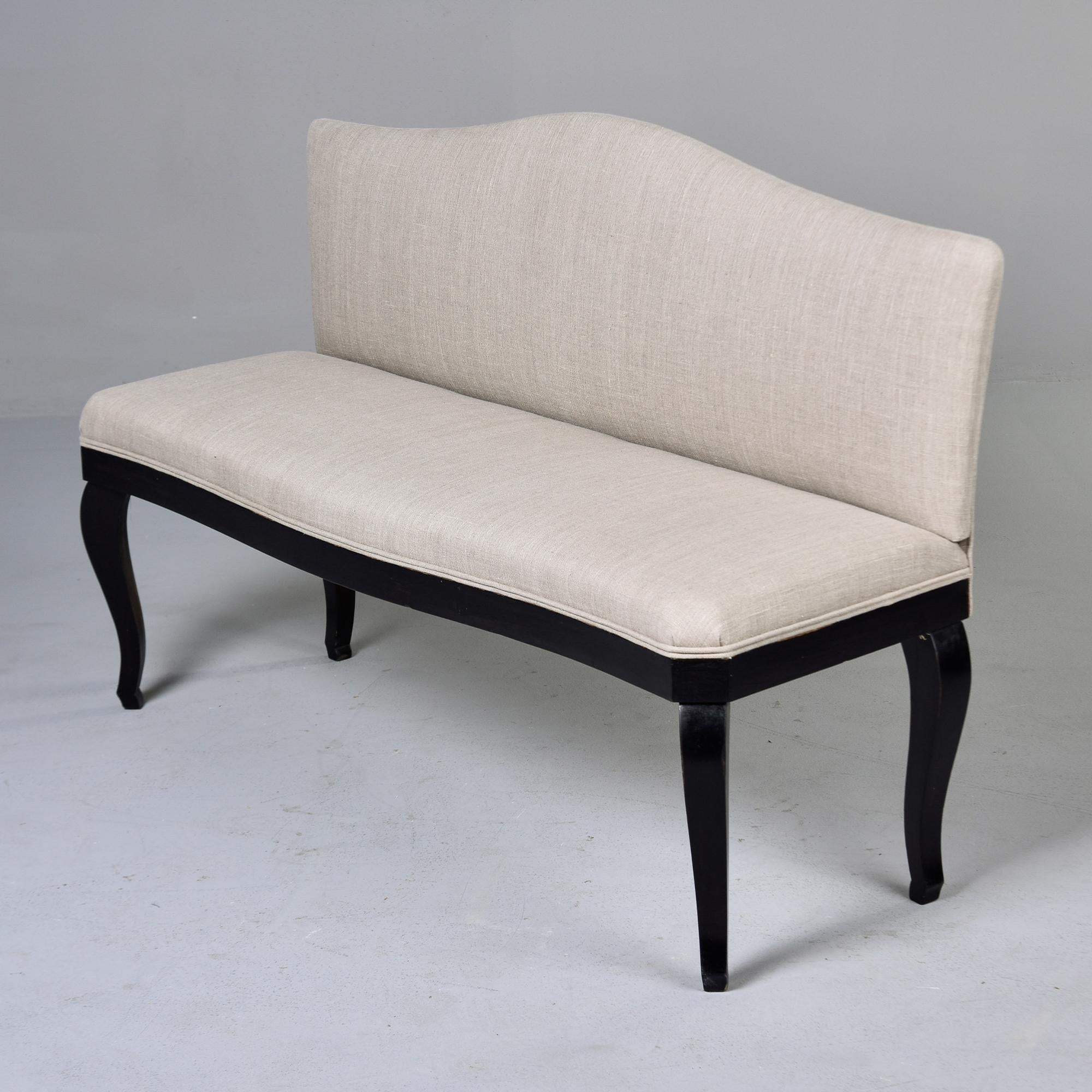 Found in France, this upholstered hall bench dates from the 1920s. Wood base and legs have ebonised finish. Bench was upholstered in natural colored linen by the dealer we acquired it from. Double welt trim along base of seat, camel back . Unknown