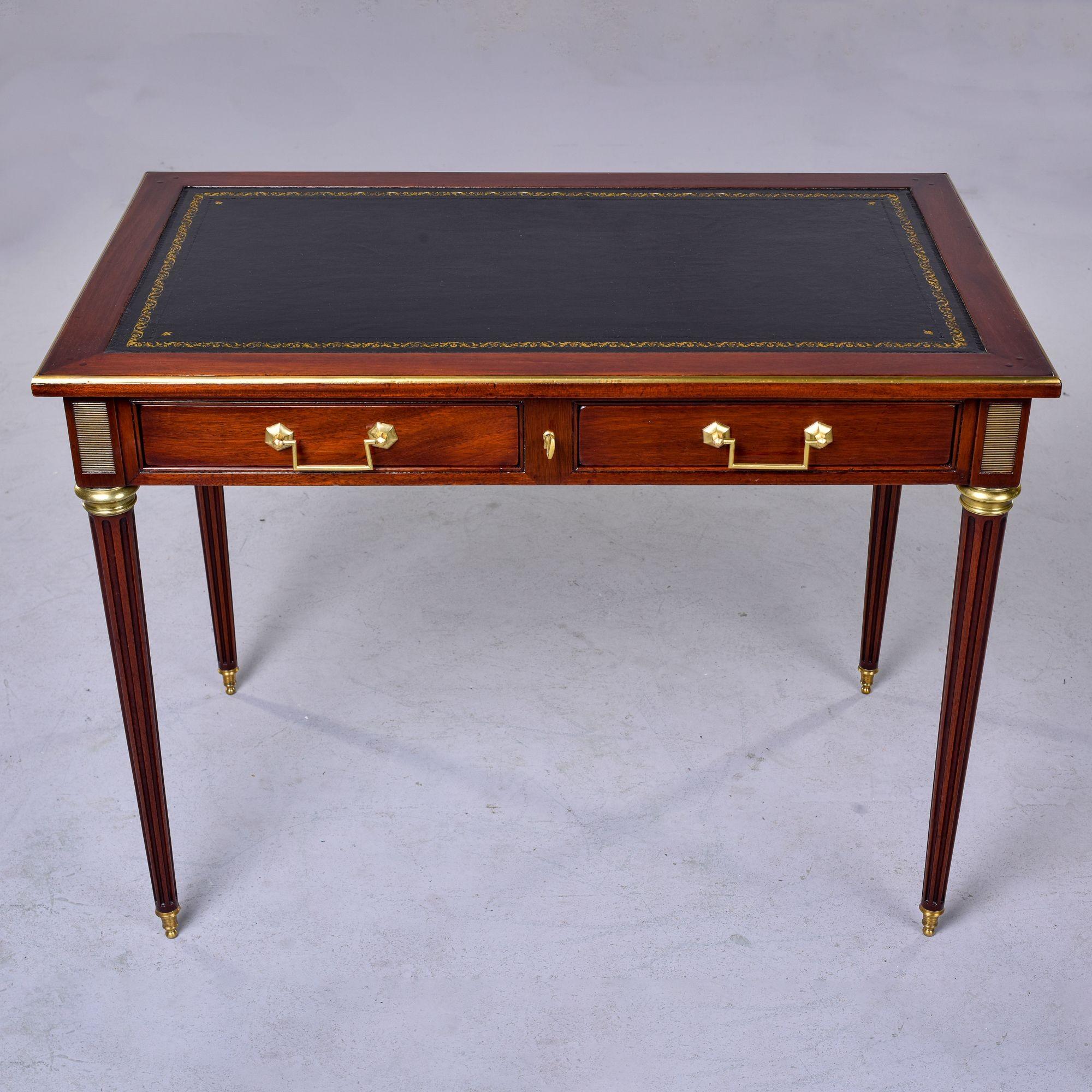 Found in France, this circa 1900 Louis Philippe style writing desk is made of mahogany. This desk features a new black leather top with gold embossed borders, decorative brass trim and hardware, two locking drawers with dovetail construction, reeded